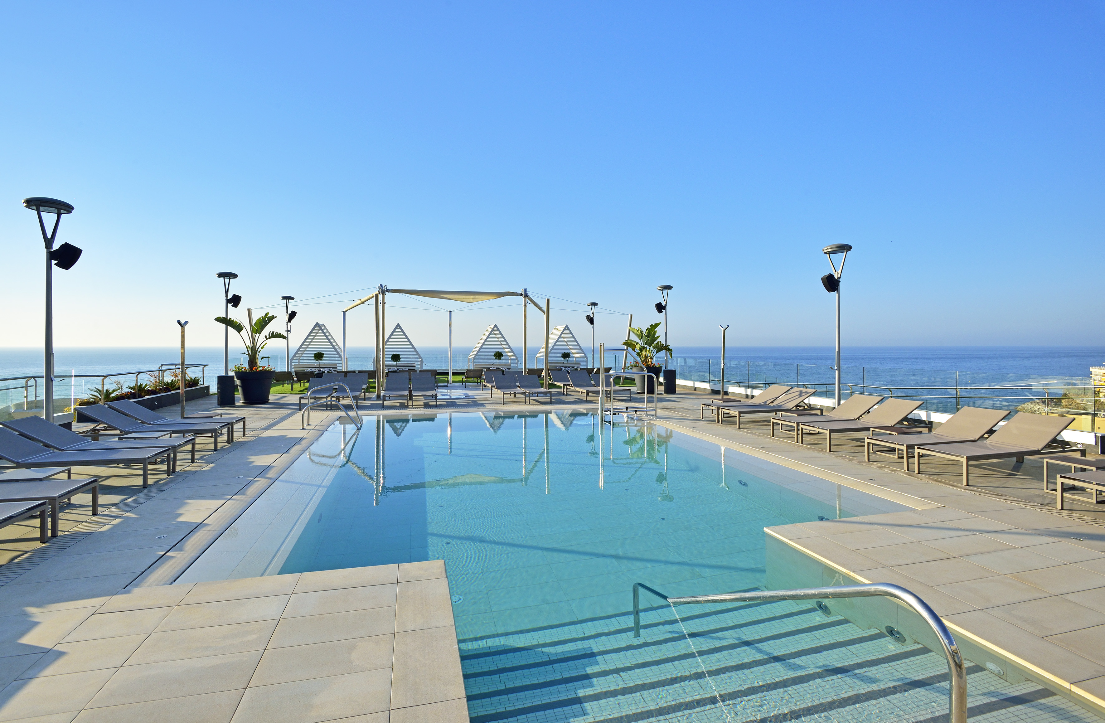 a pool with chairs and a deck chair on a rooftop overlooking the ocean