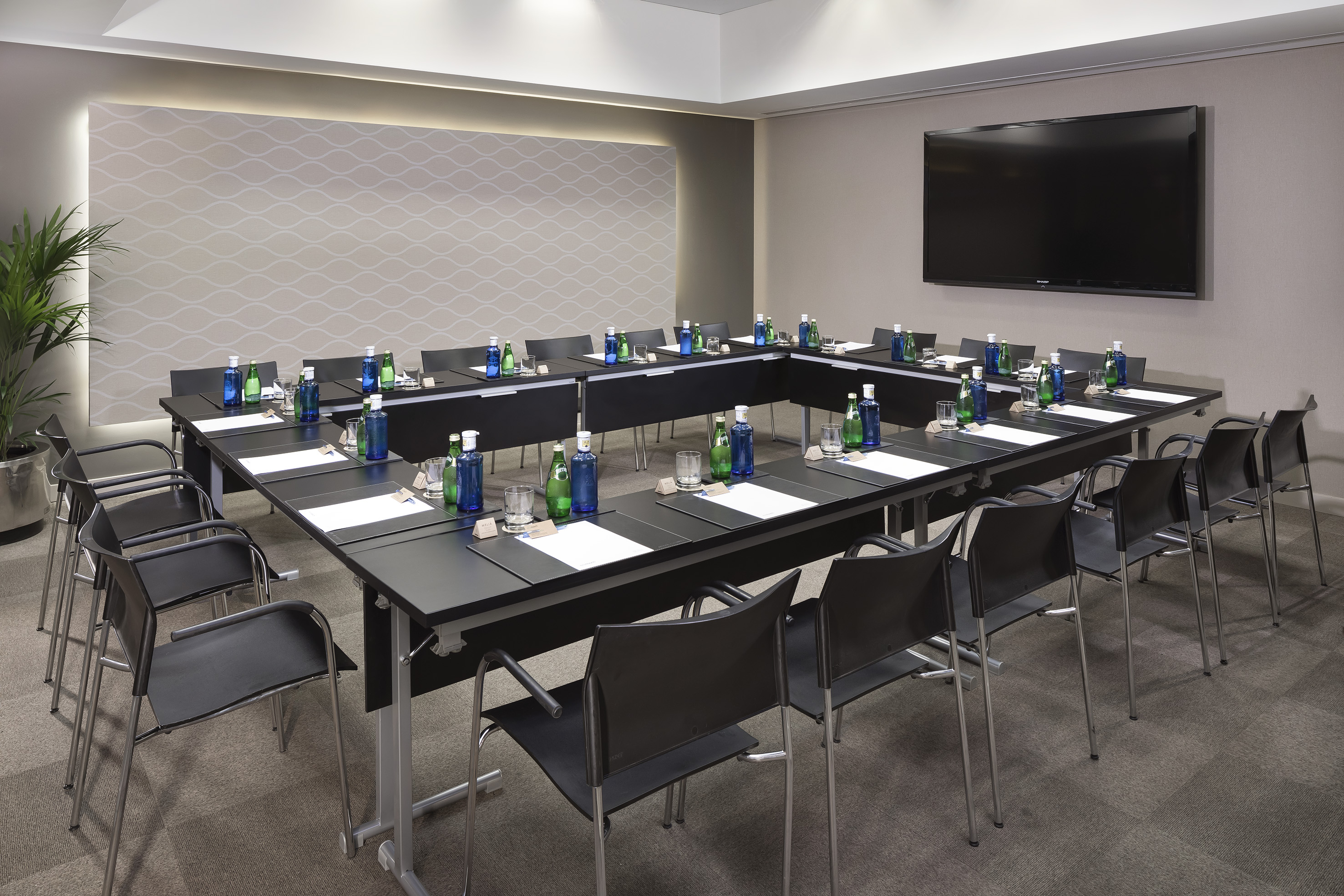 Professional U-shape conference room with black tables, chairs, and large TV.