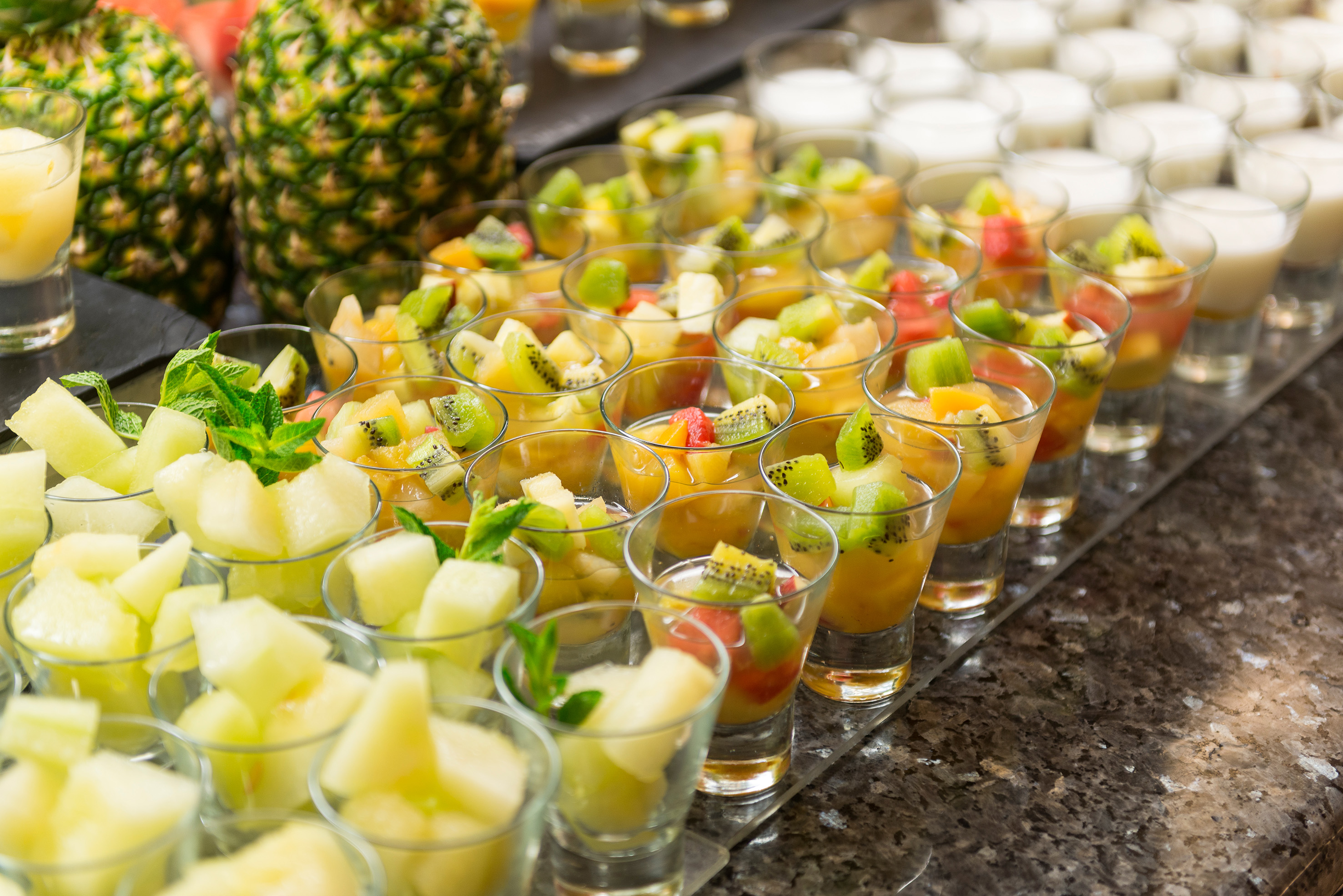 Fresh fruit salad shots: kiwi, melon, mint, yogurt, displayed with pineapples.