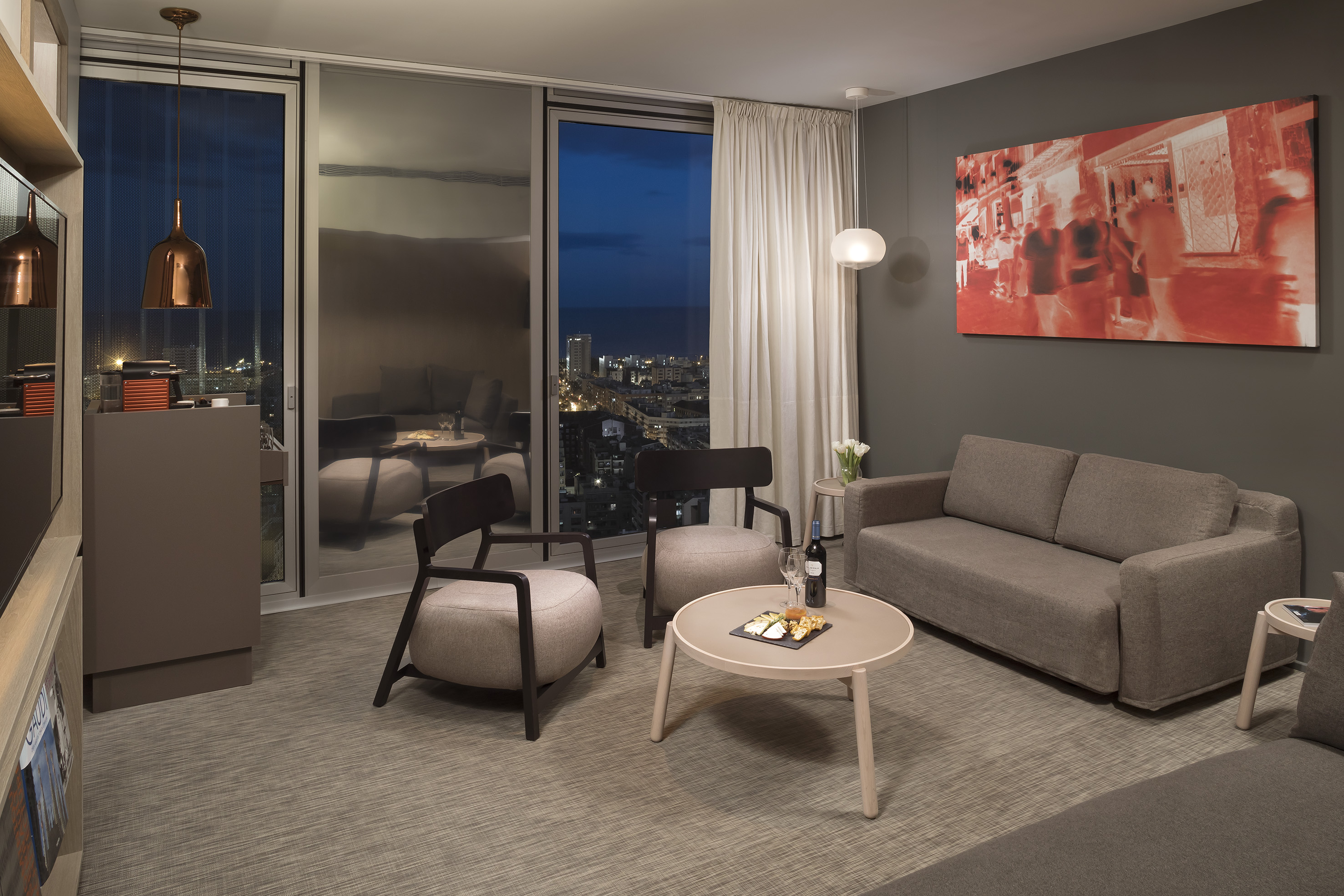 Modern living room with city night view, sofa, armchairs, and coffee table.