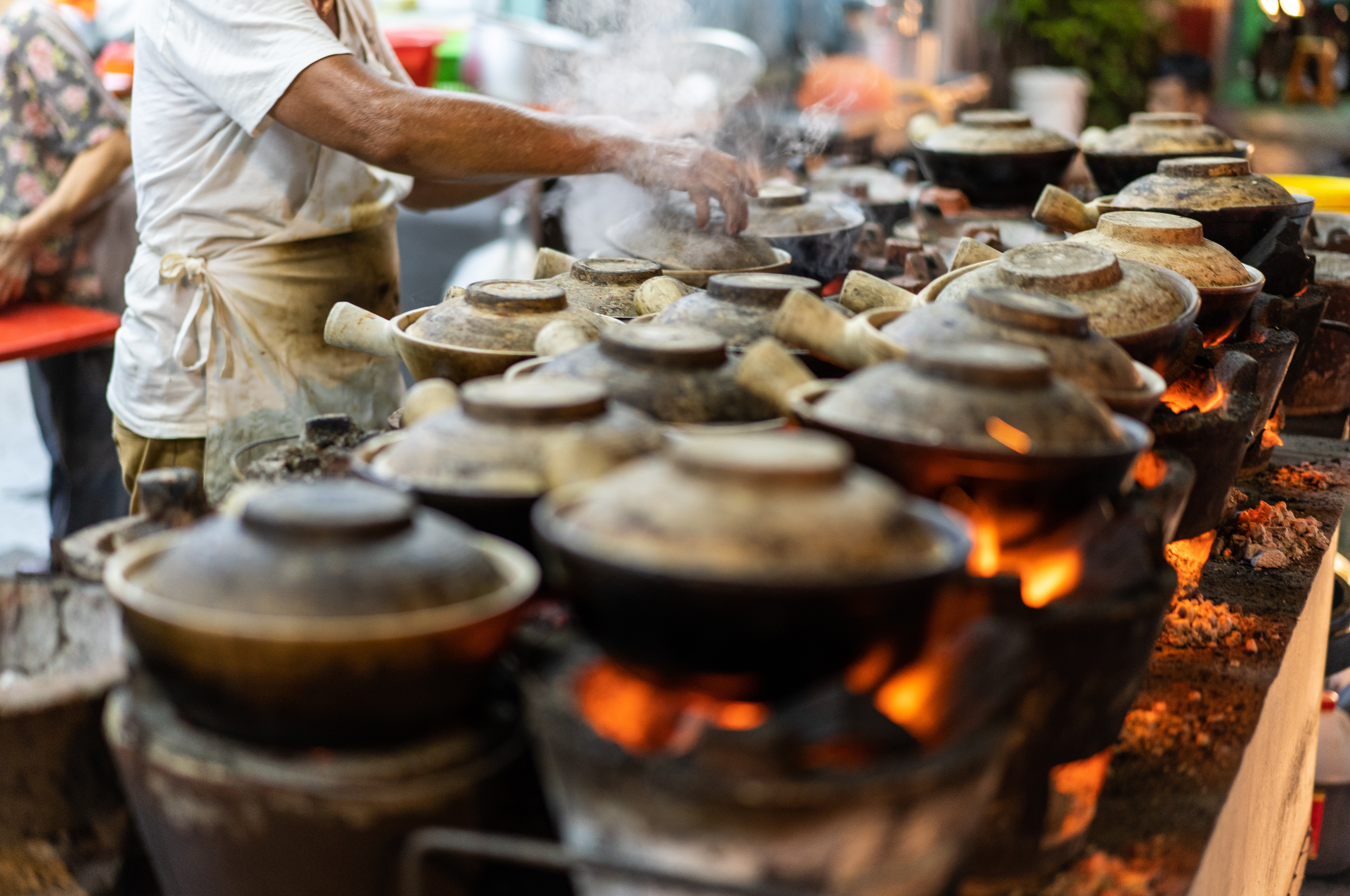 Claypot rice steaming on charcoal stoves, chef cooking at a hawker stall.