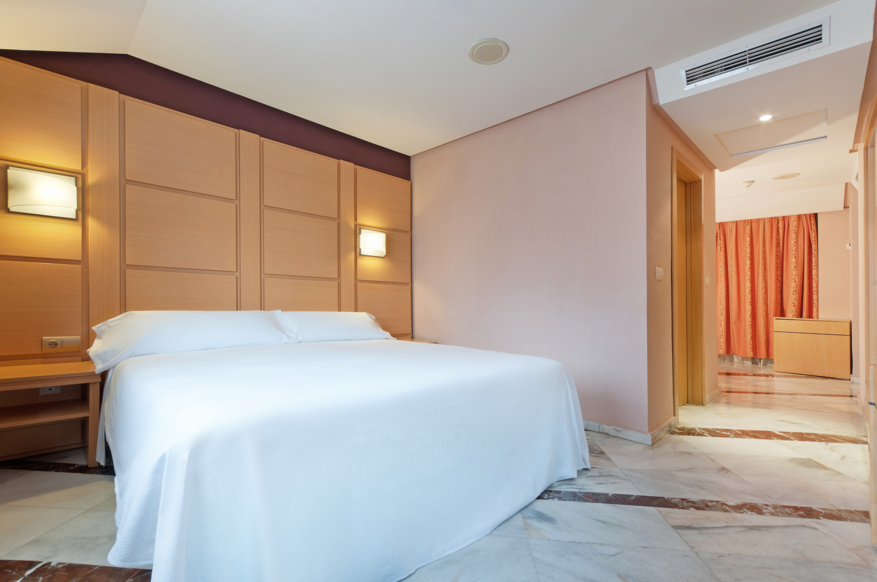Modern hotel bedroom with white bed, wooden headboard, and marble floor.