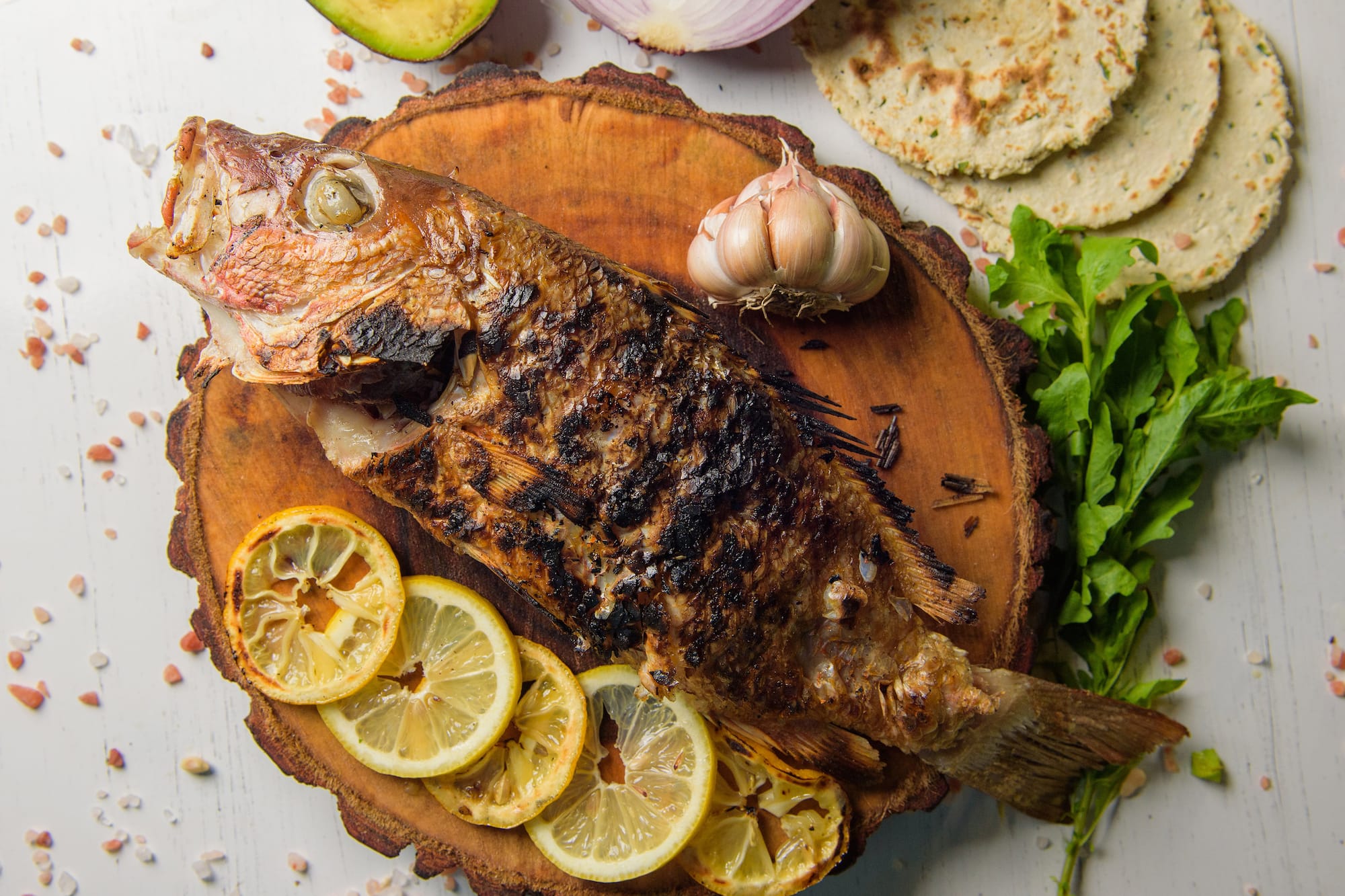 Pescado asado entero con limón, ajo, aguacate, tortillas y cebolla.