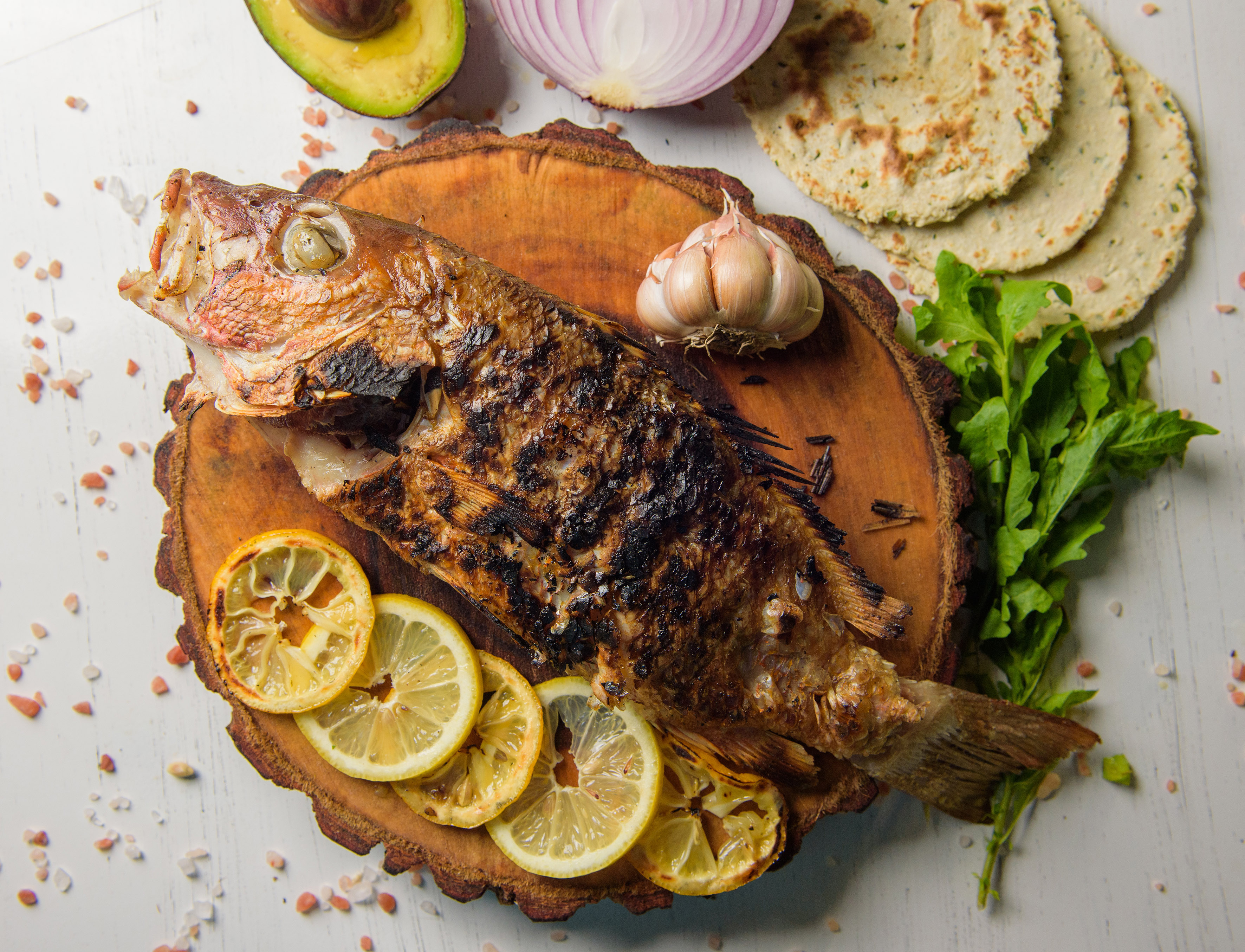 Pescado asado entero con limón, ajo, aguacate, tortillas y cebolla.