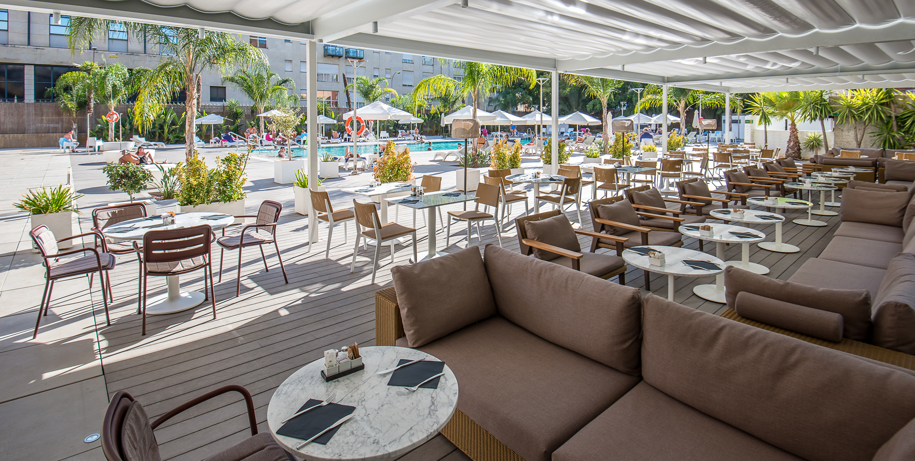 Outdoor resort dining patio with lounge seating overlooking a sunny pool.