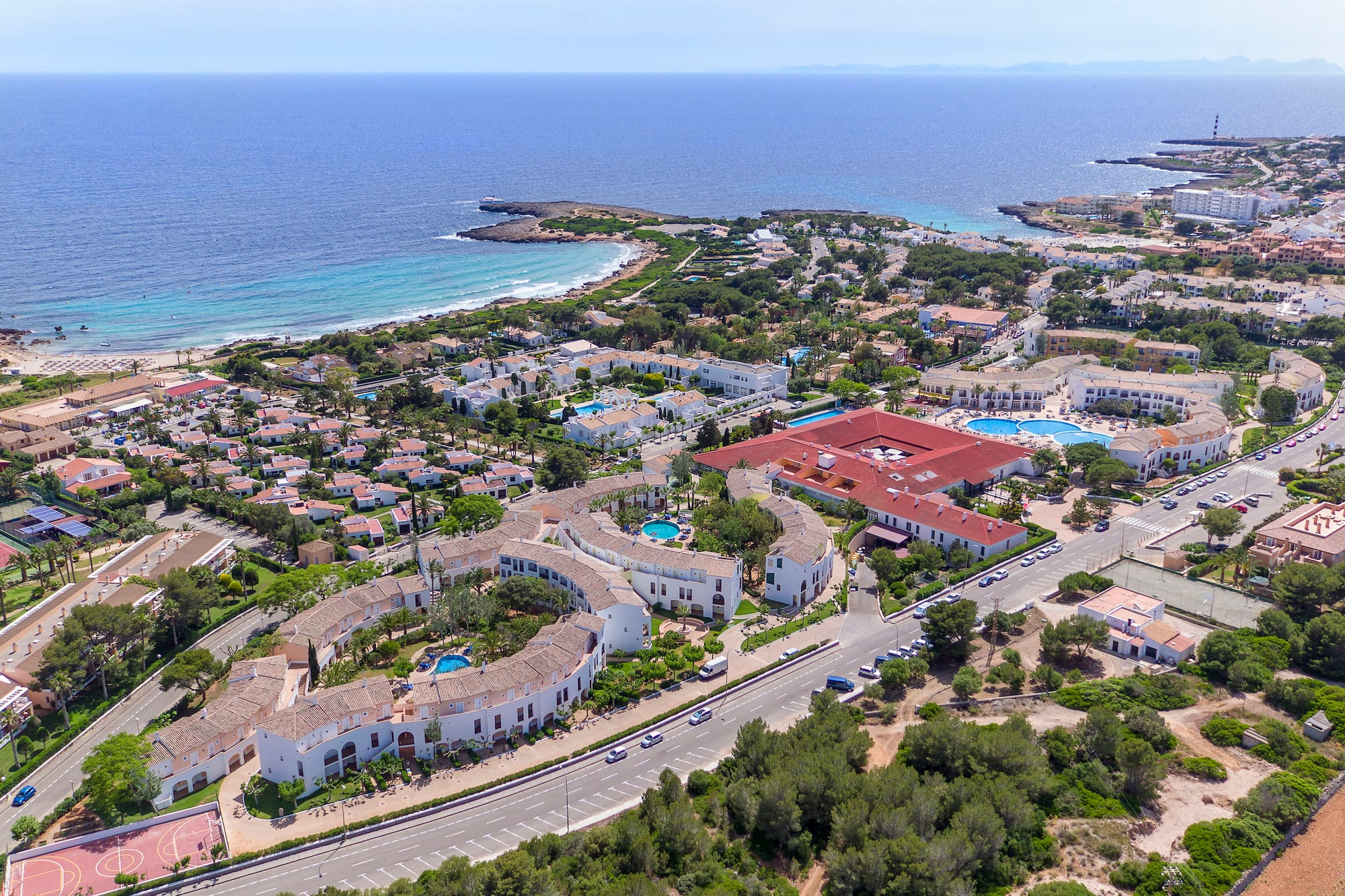 Sunny Mediterranean coastal resort: aerial view of hotels, pools, and beach.