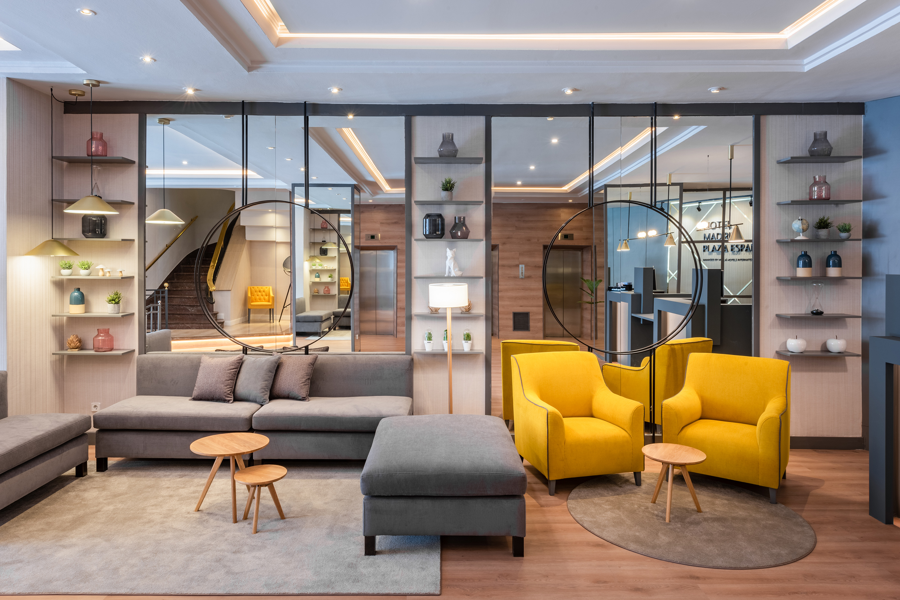 Modern hotel lobby: gray sofa, yellow armchairs, decorative shelves, mirrors.