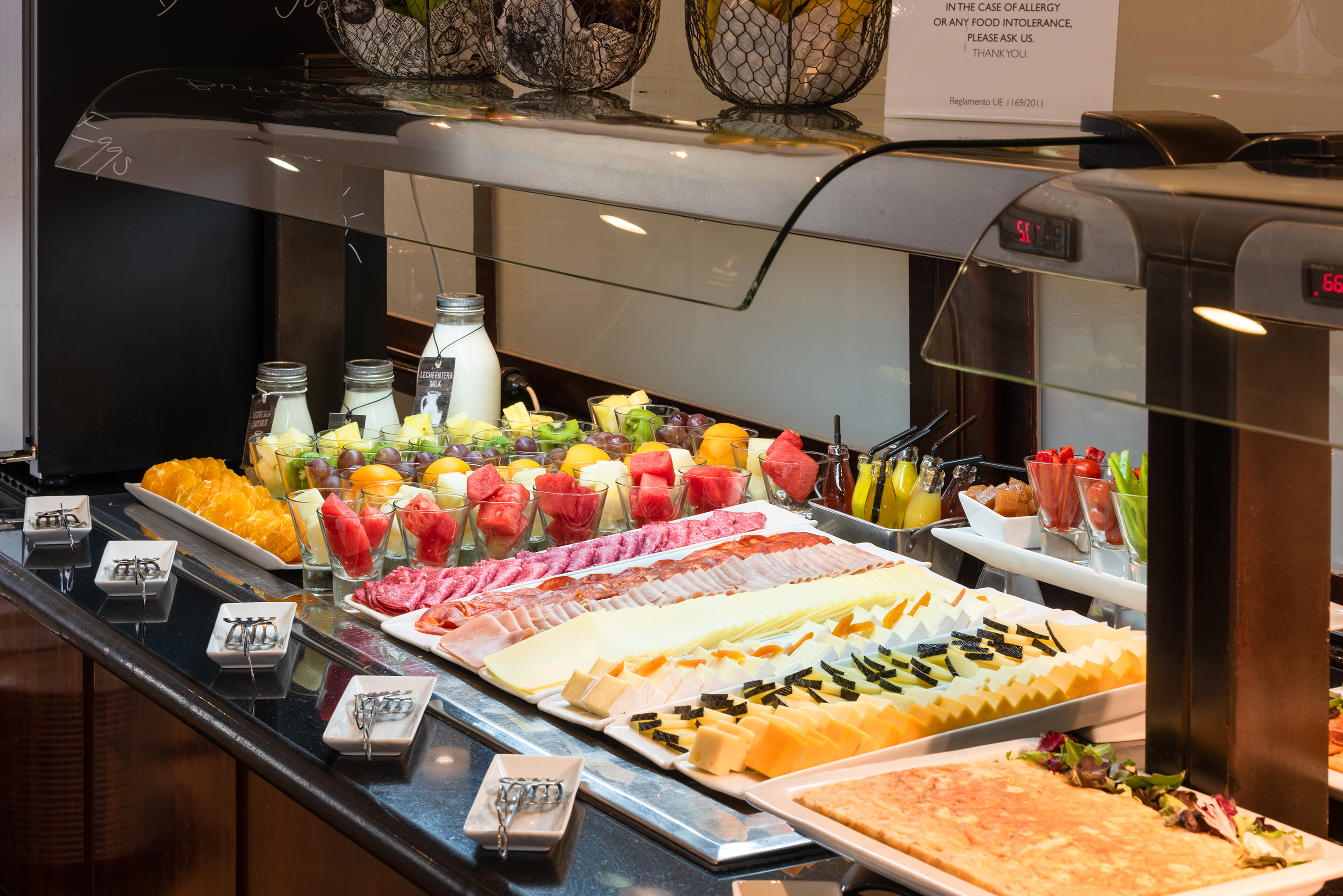 Hotel breakfast buffet with fresh fruit cups, sliced cheese, and cold cuts.