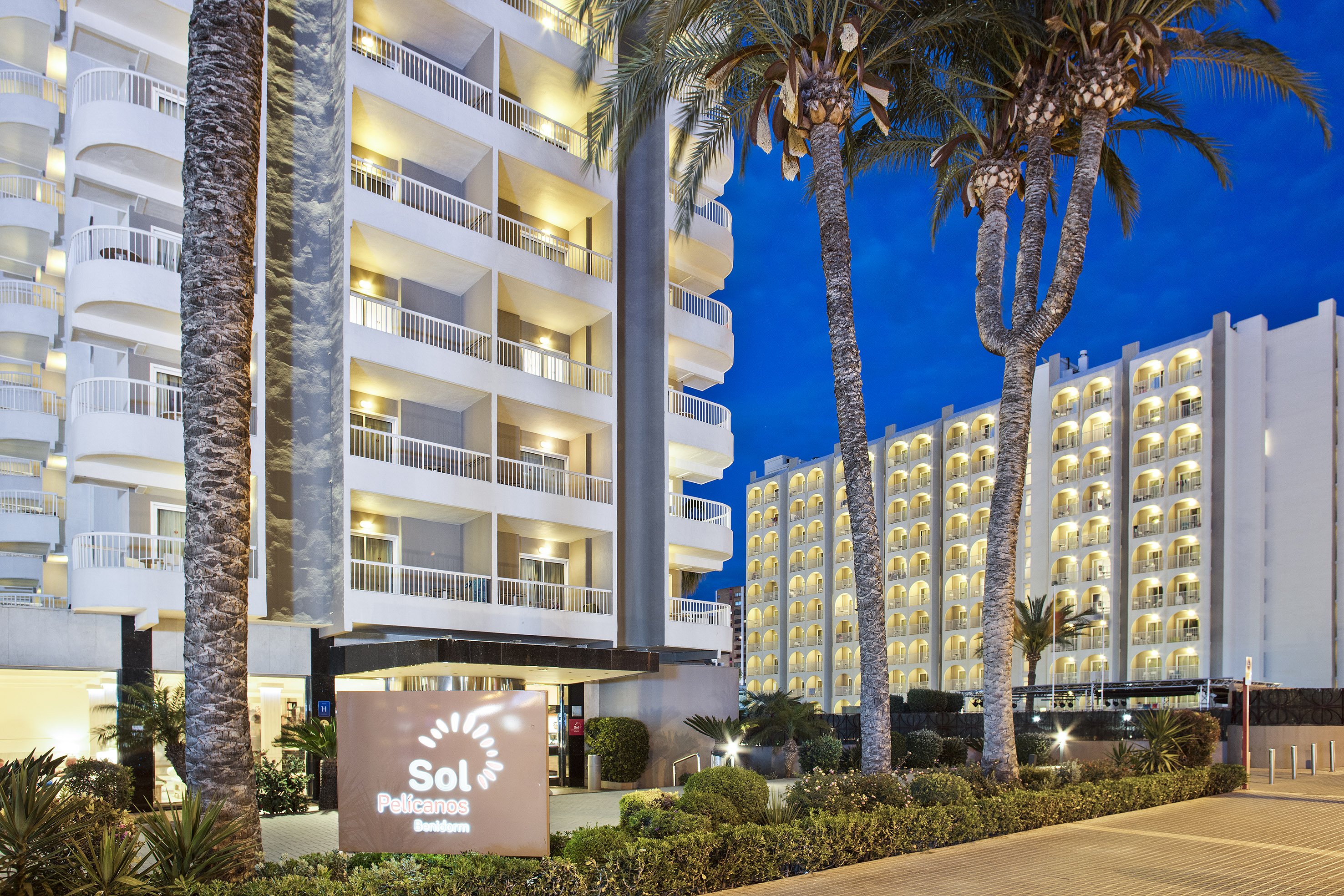 Sol Pelícanos Benidorm hotel exterior at dusk, illuminated balconies, palm trees.