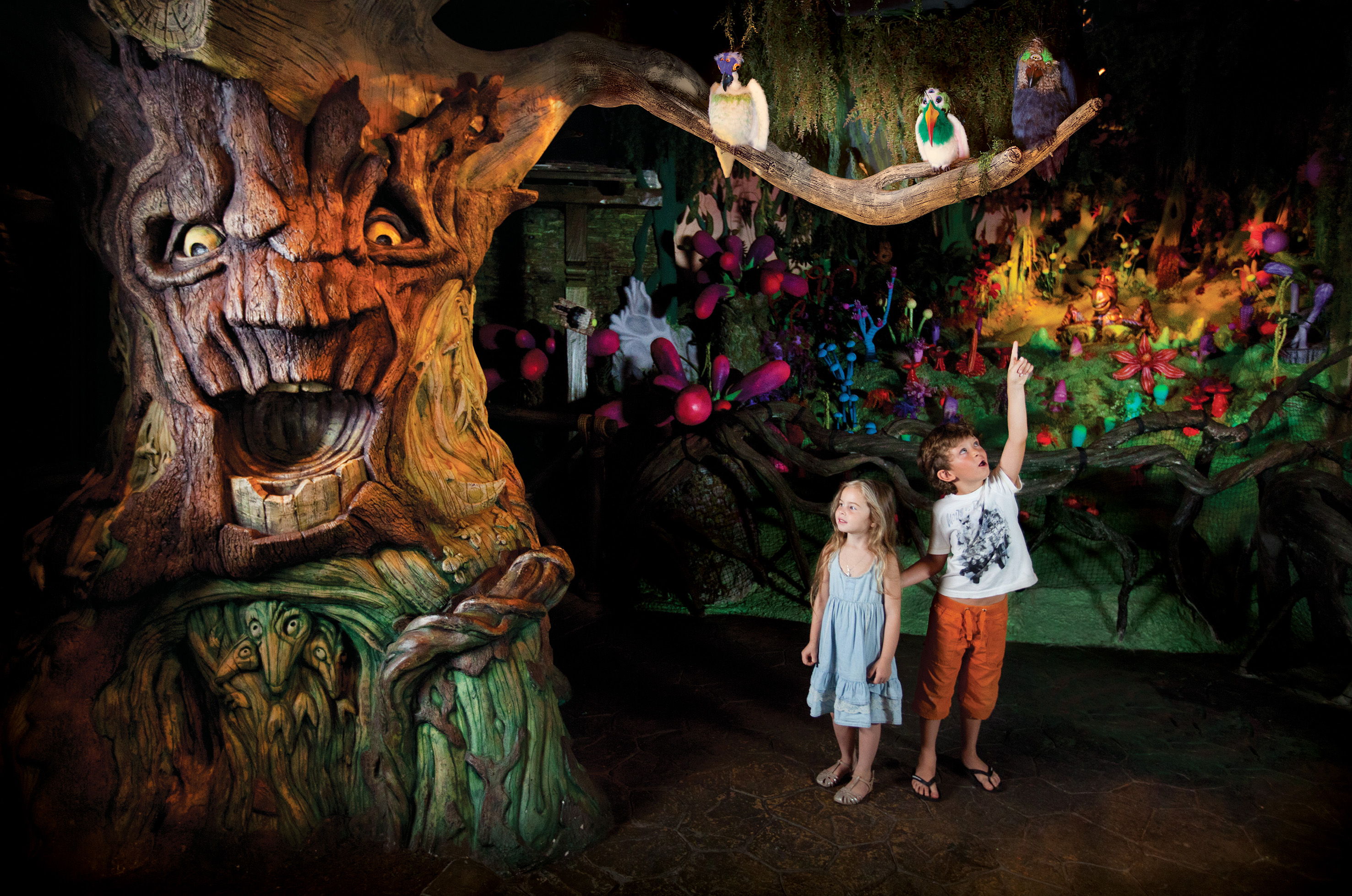 Kids gaze at a fantasy talking tree in a whimsical forest theme park.