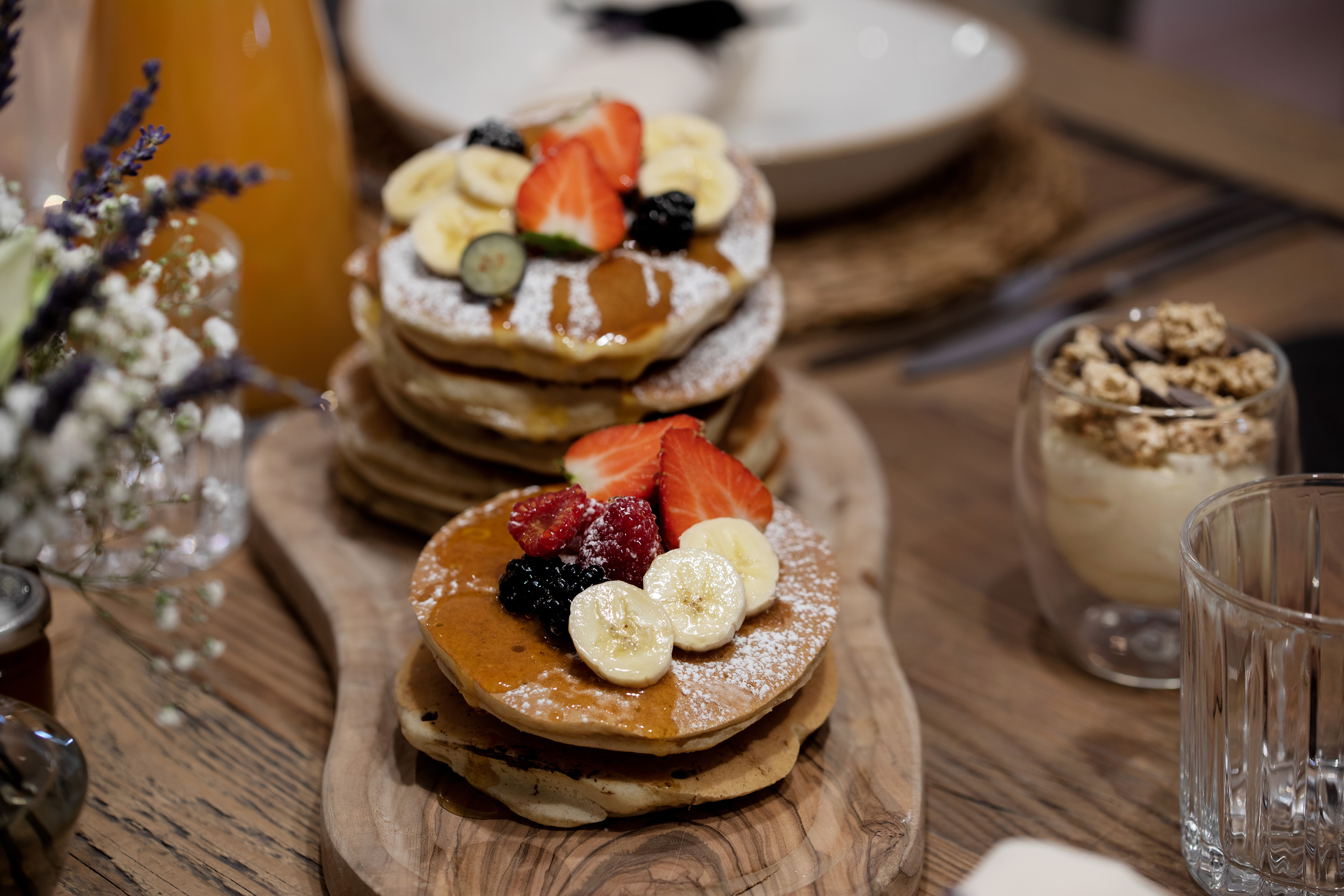 Breakfast pancakes with berries, banana, syrup, and powdered sugar.