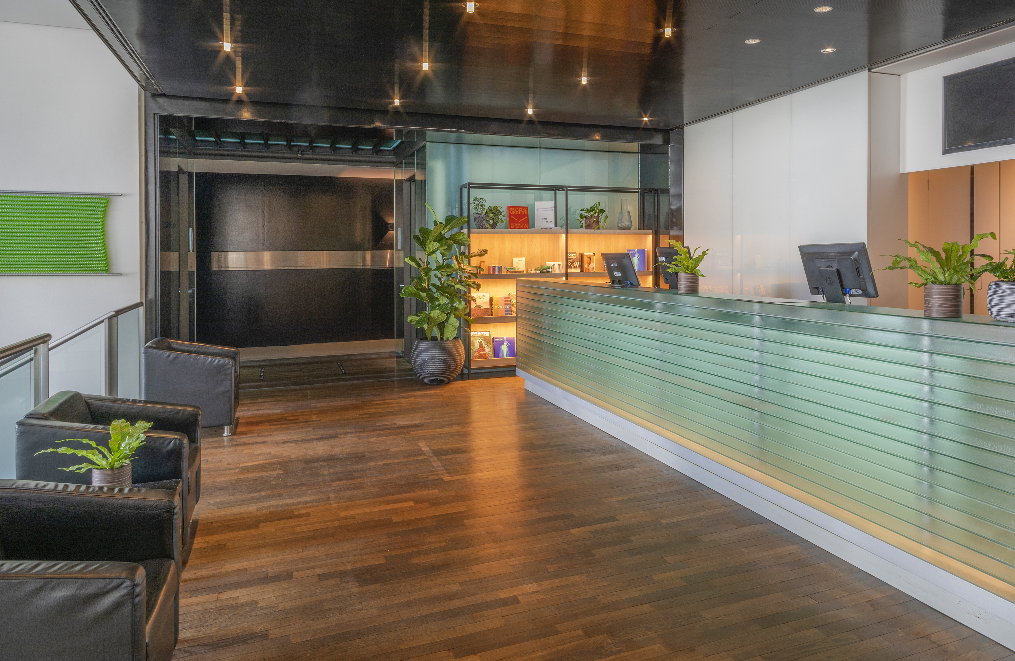 Modern reception area with green desk, plants, black chairs, and wood floor.