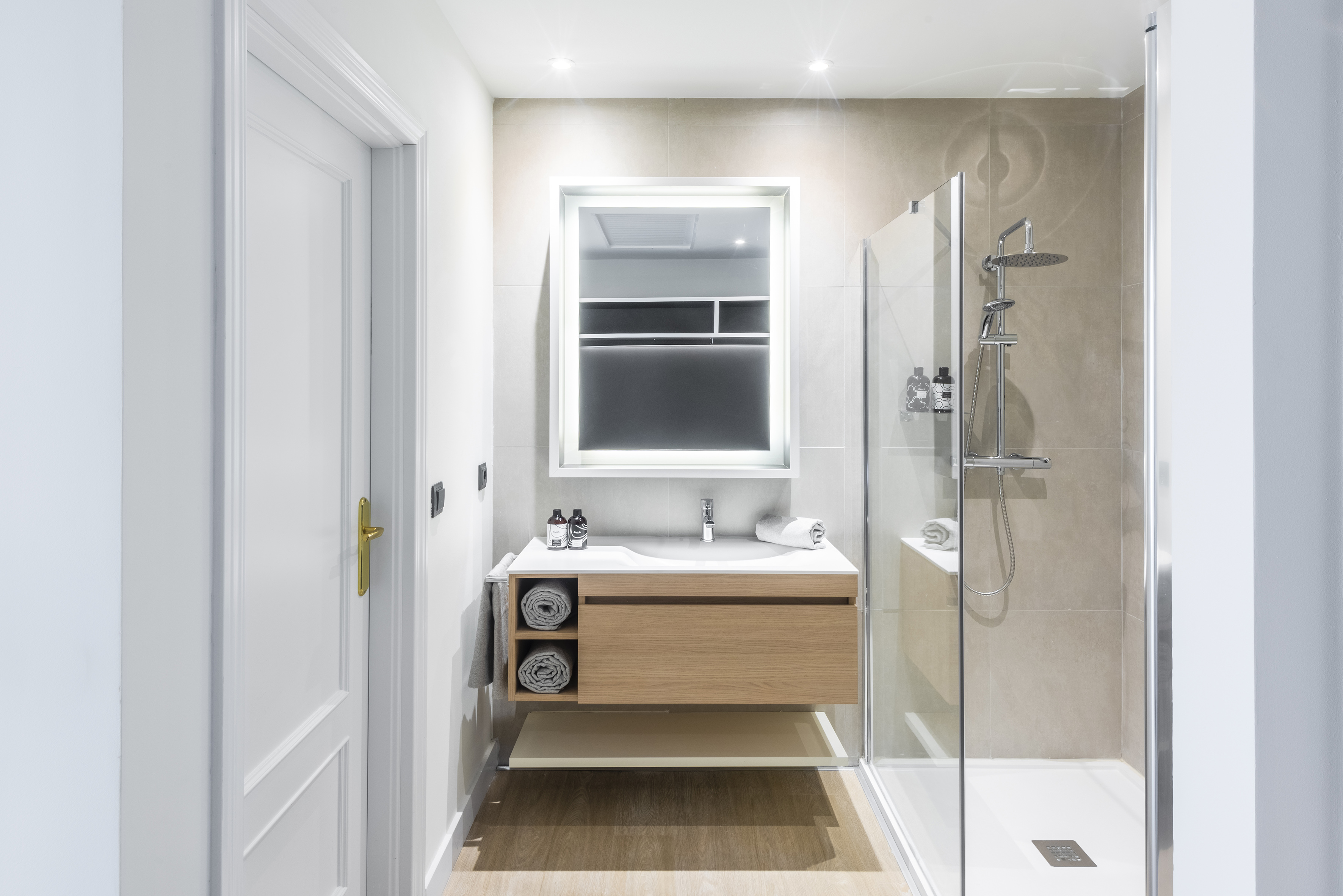 Modern bathroom with wood vanity, backlit mirror, and glass shower.