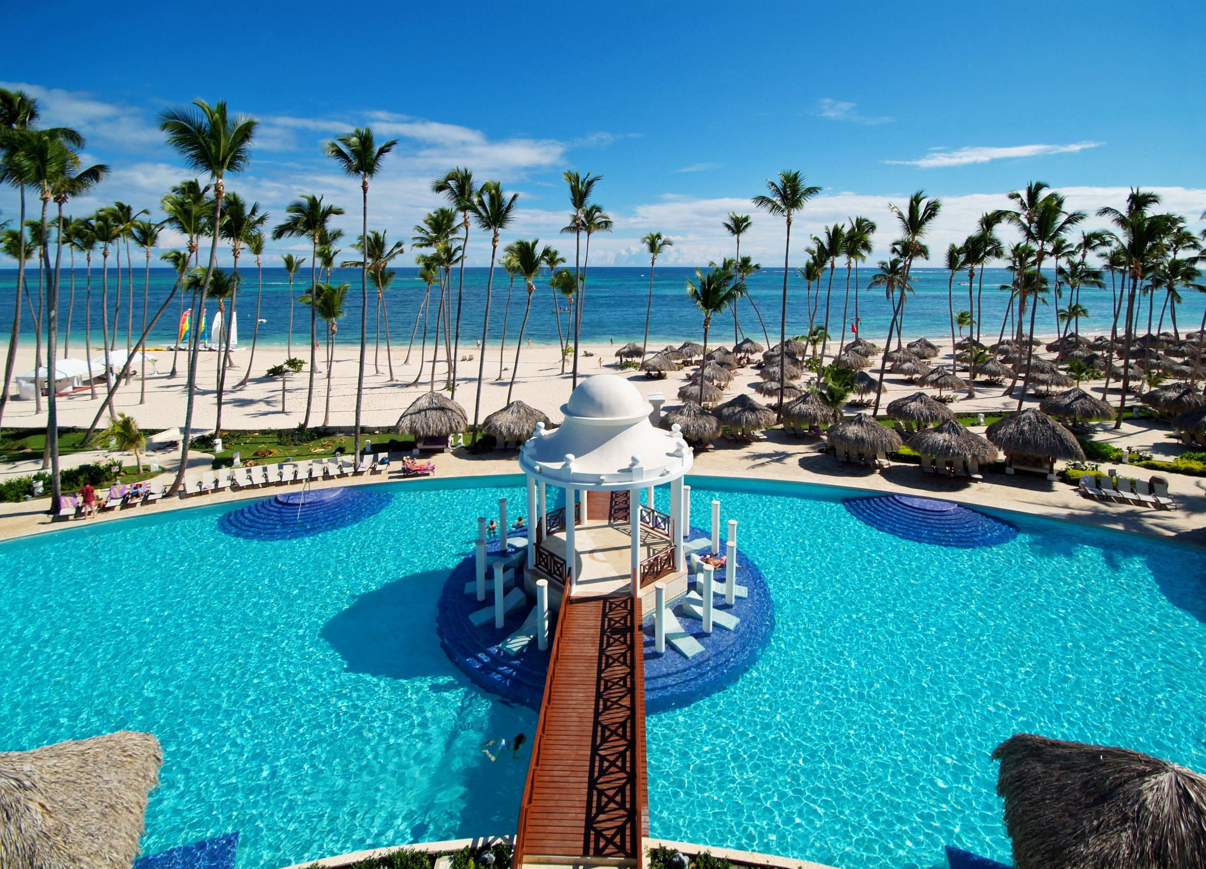 Tropical resort pool with swim-up gazebo, palm trees, and sandy beach.