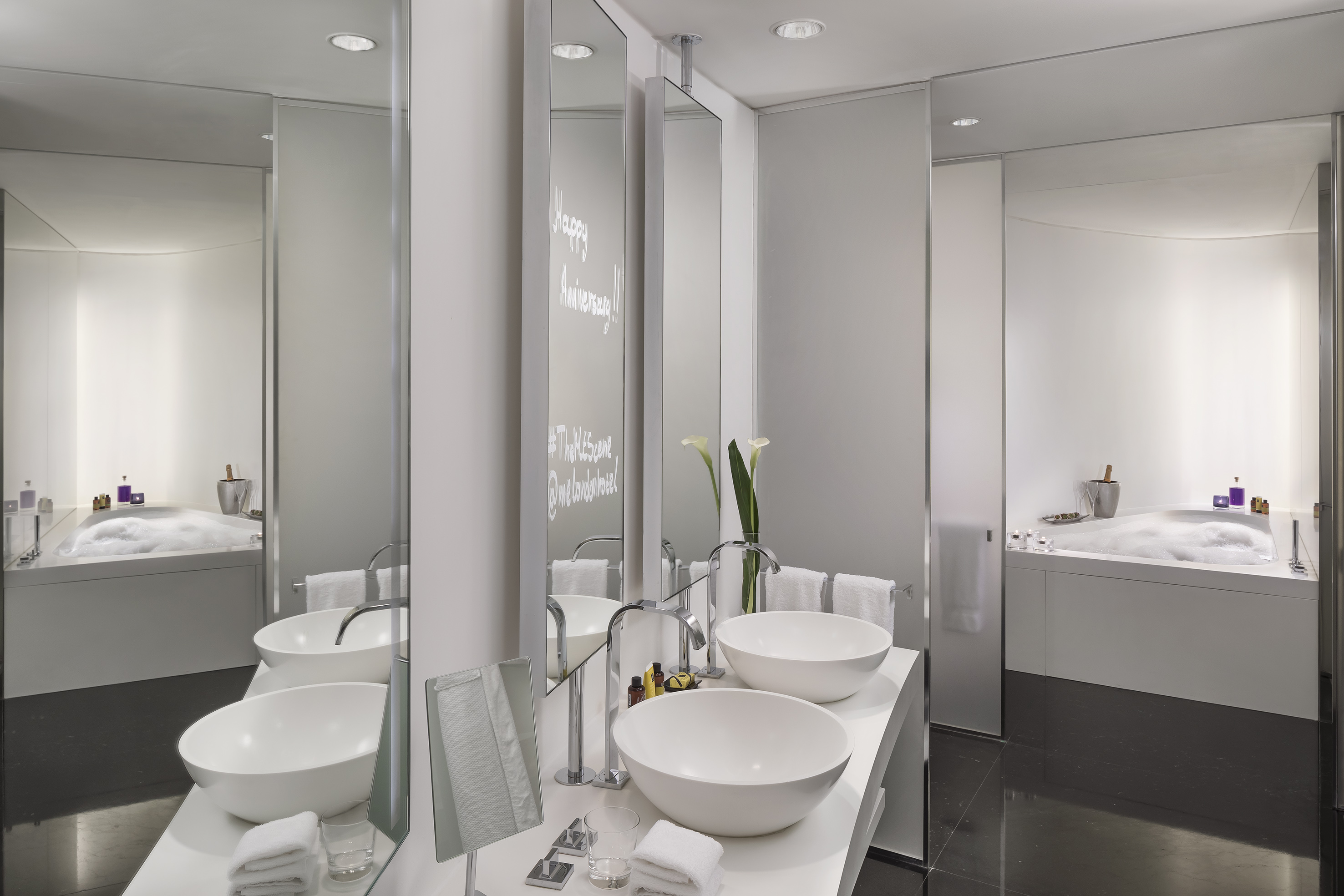 Sleek modern hotel bathroom with double vanity, bowl sinks, and bubbly bathtub.