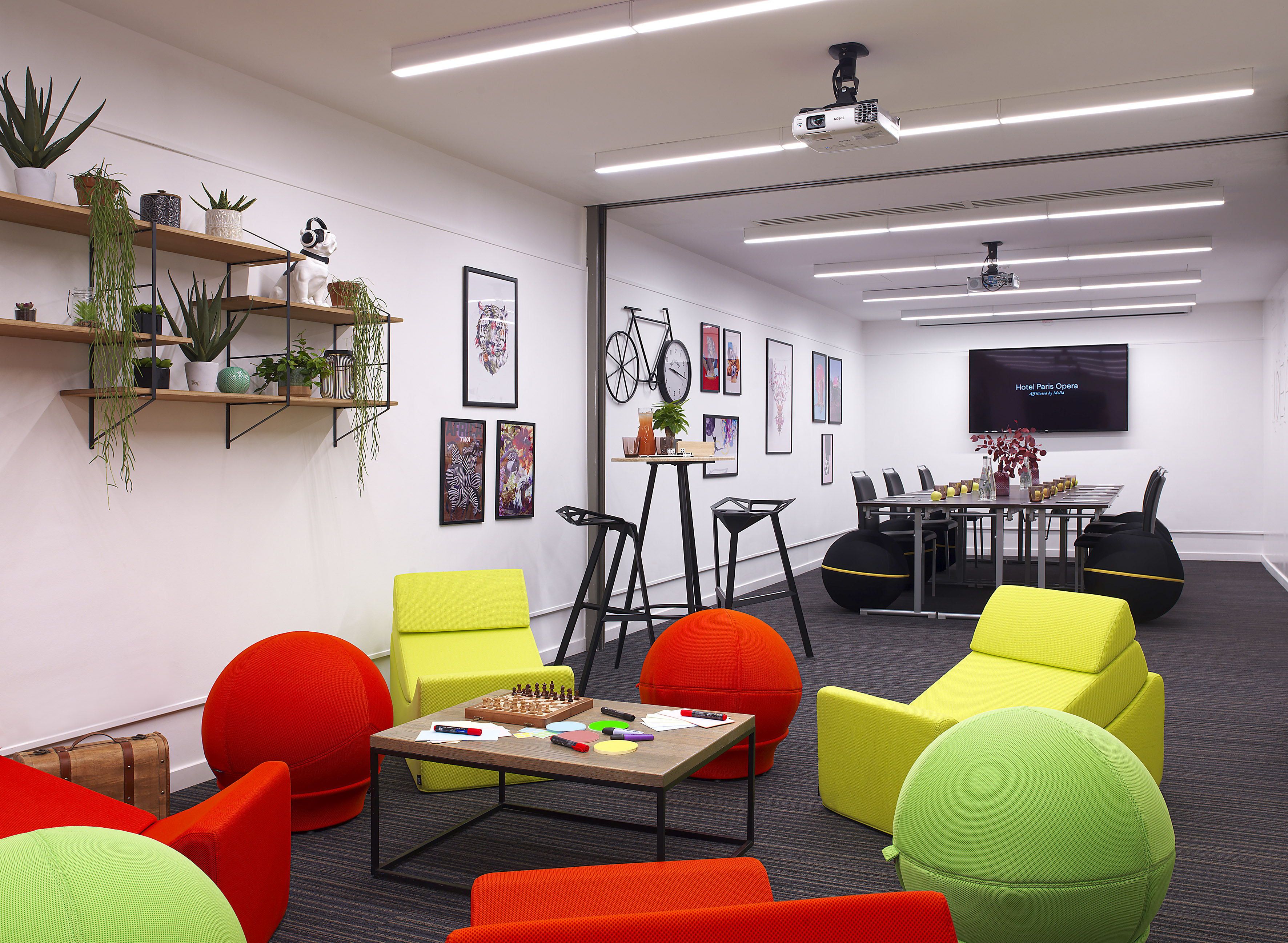 Vibrant modern hotel meeting lounge with colorful furniture and conference screen.