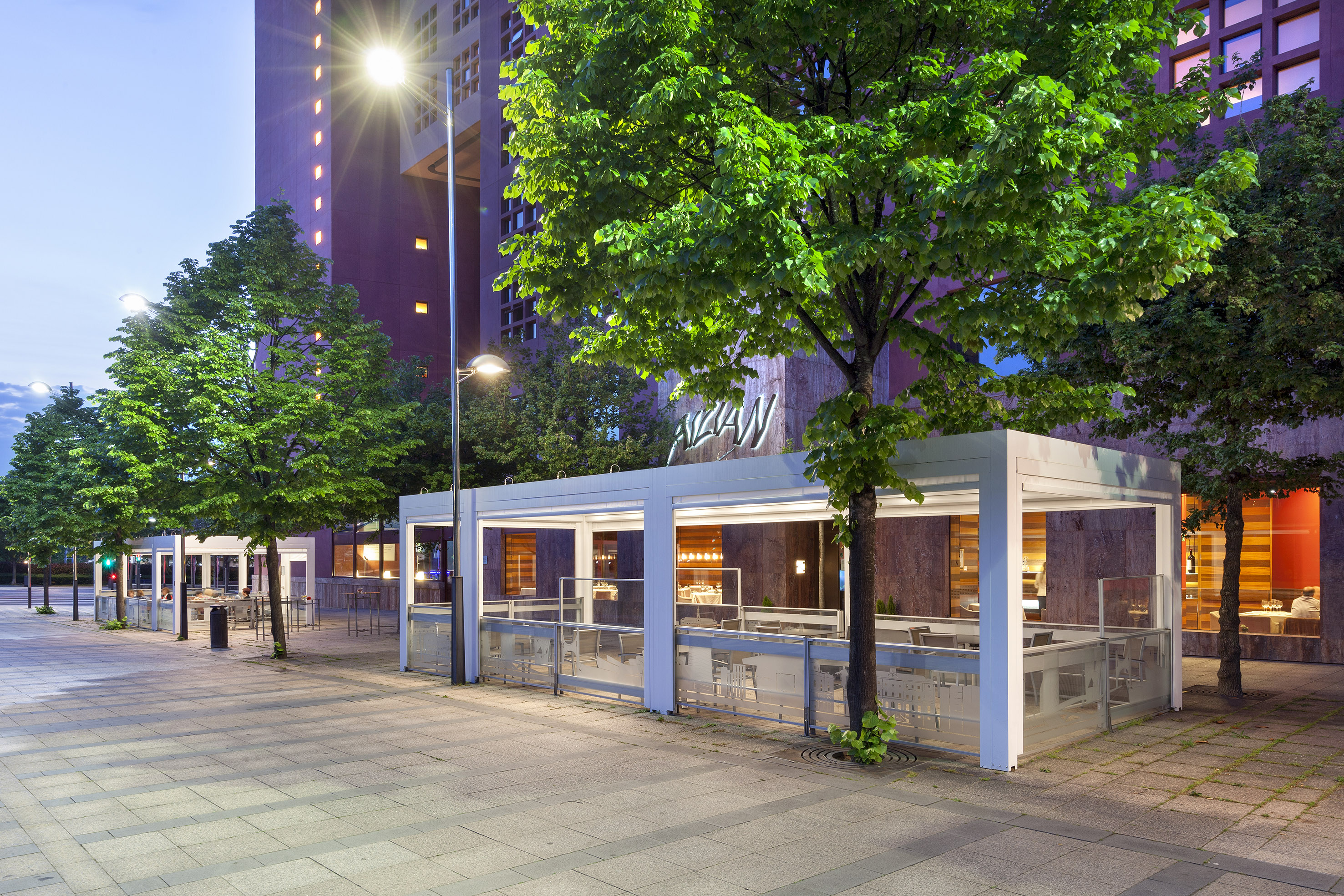 Modern restaurant patio with white pergola on a city street at dusk.