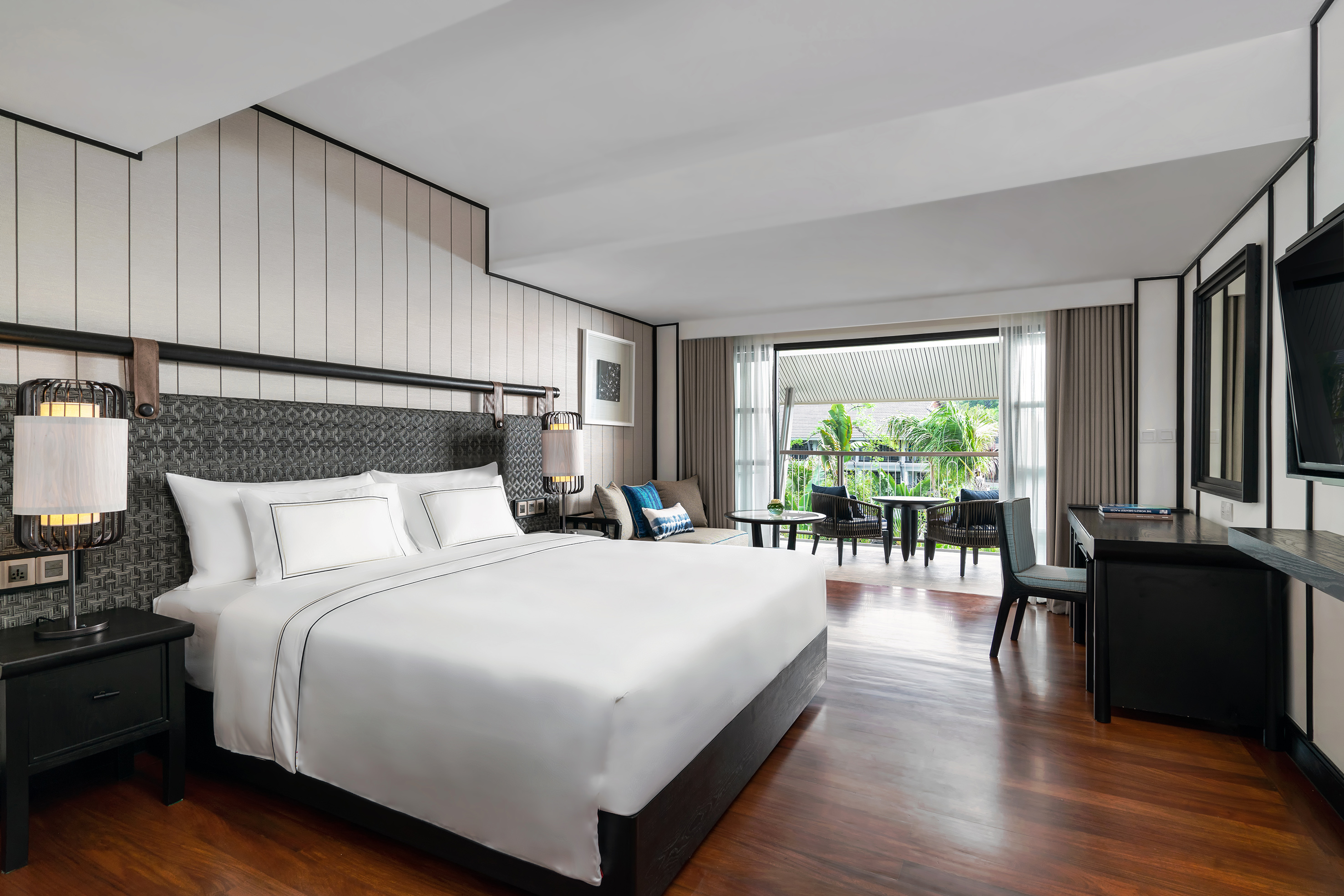 Luxury hotel bedroom with king bed, desk, balcony, and tropical view.