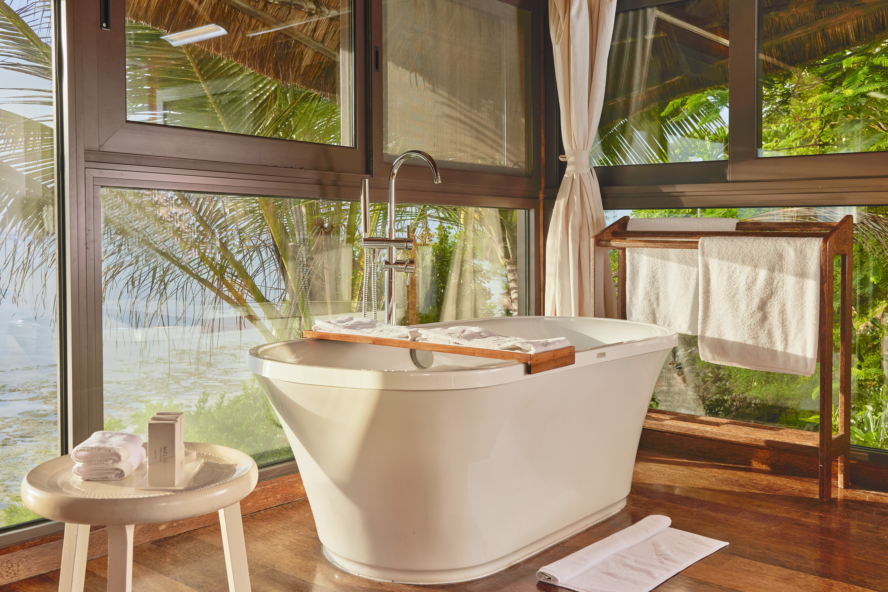 Elegant tropical bathroom with freestanding tub and ocean view windows.
