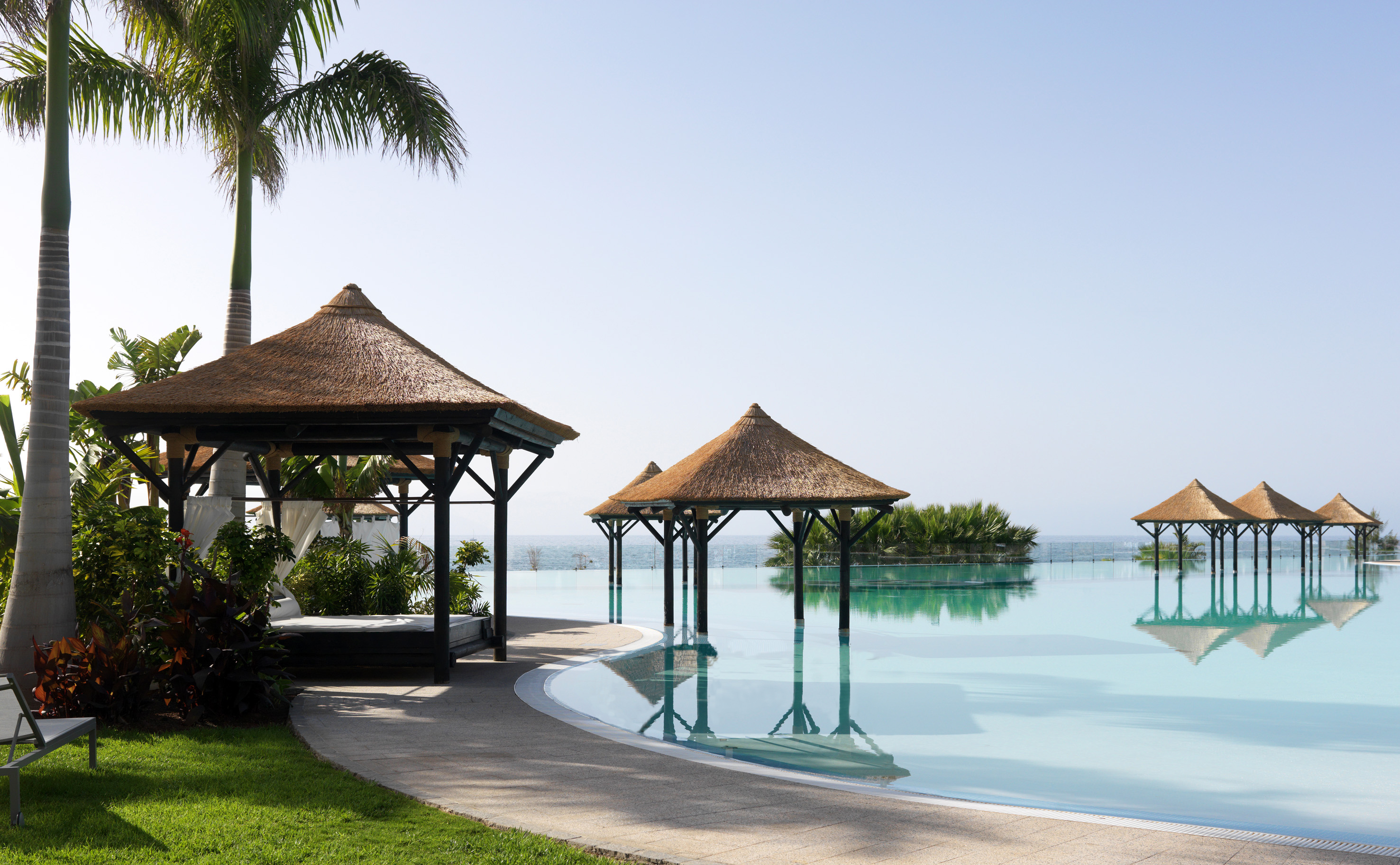 Luxury resort infinity pool with thatched gazebos, palm trees, and ocean view.