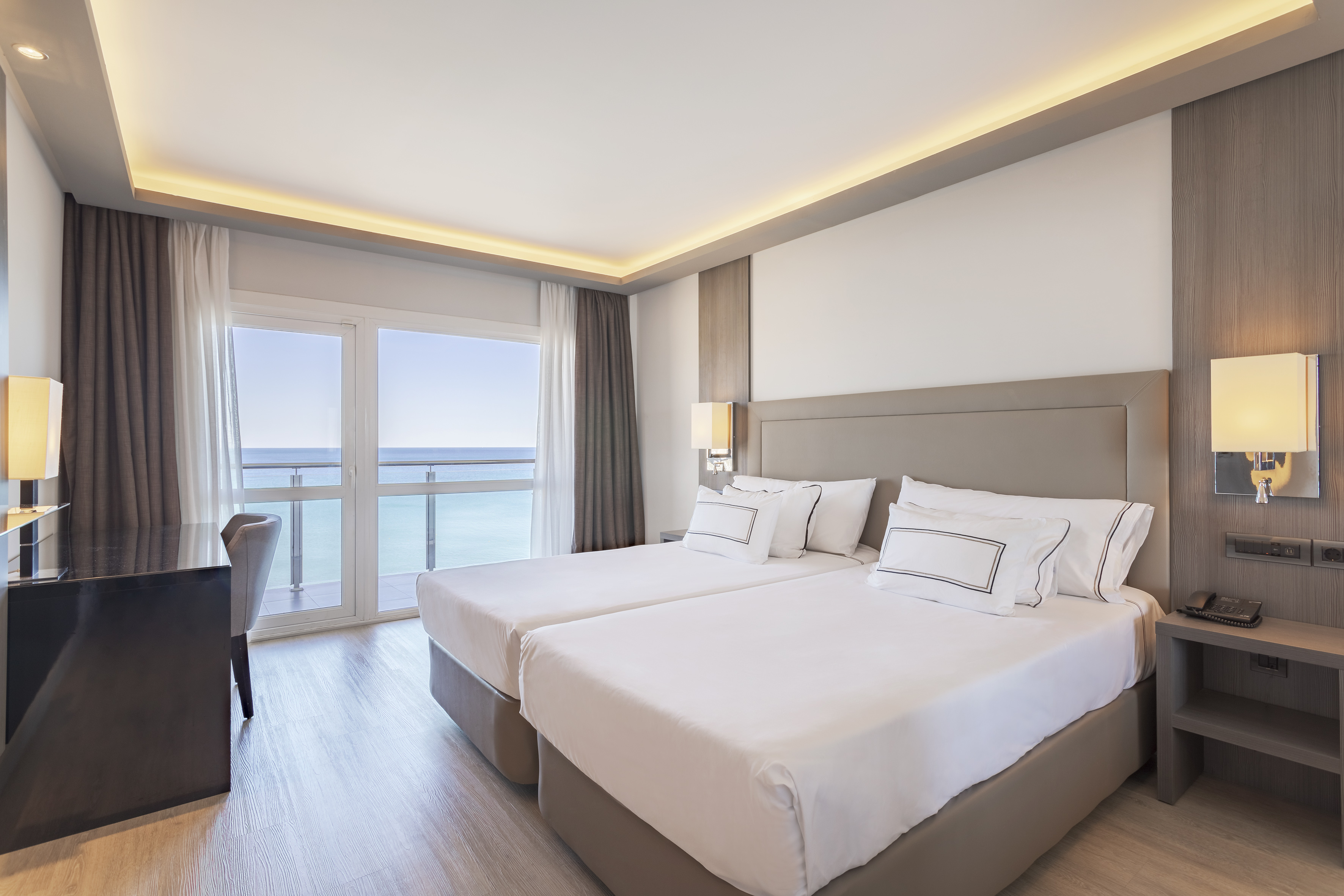 Coastal hotel room with twin beds, balcony, and ocean views.