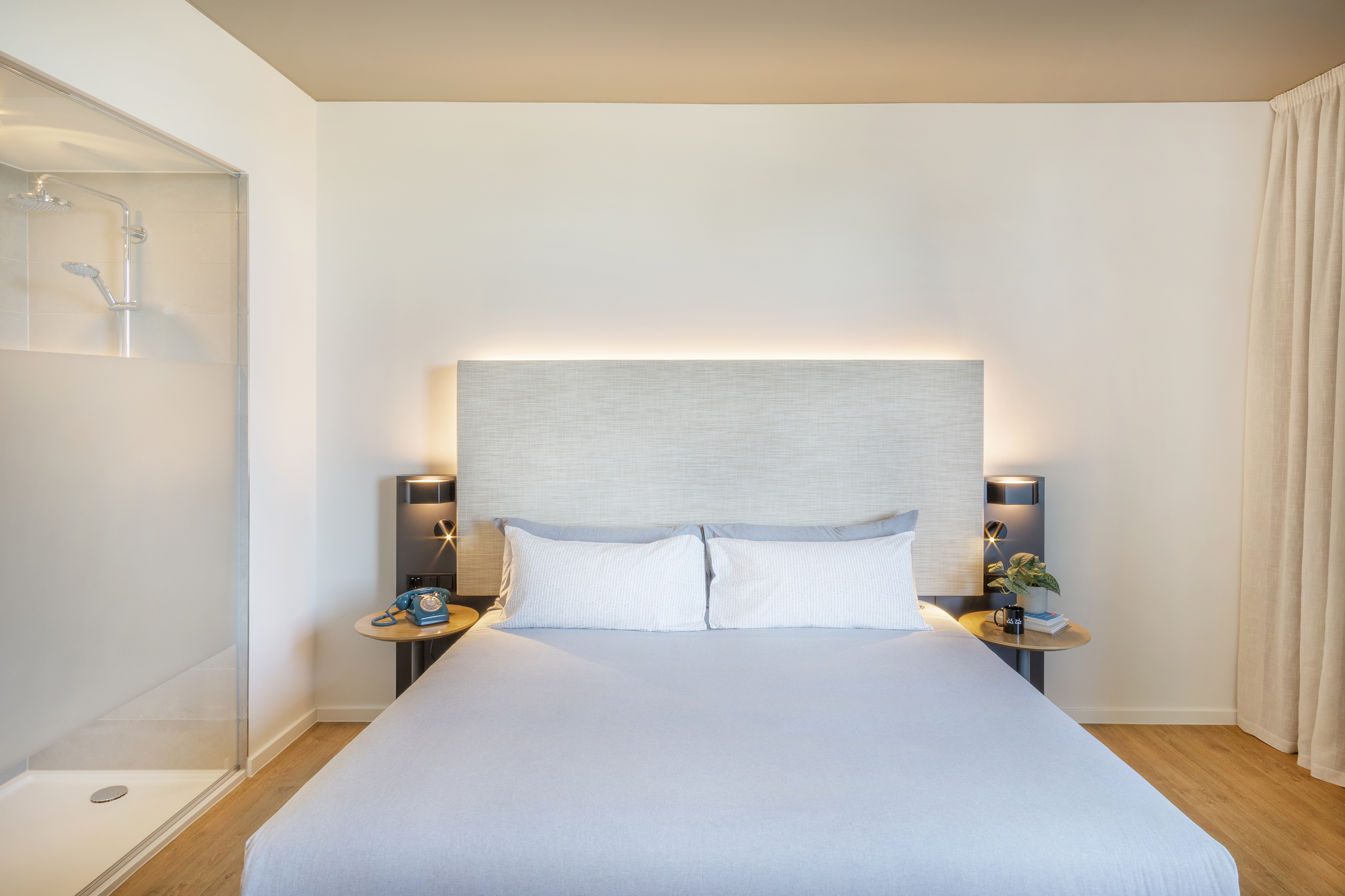 Bright modern hotel room with bed, illuminated headboard, integrated shower.