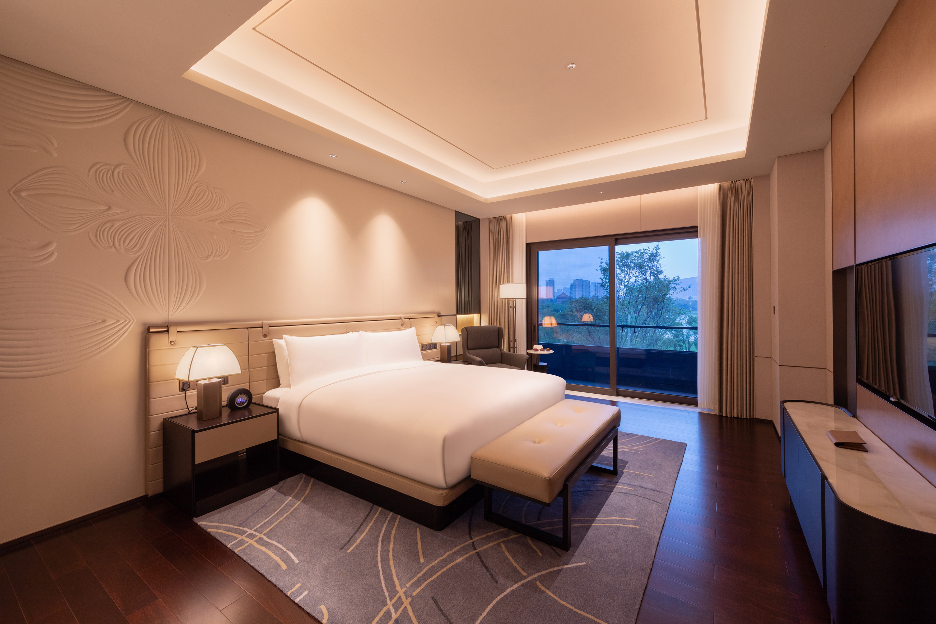 Spacious hotel bedroom with king bed, modern decor, and balcony view at dusk.