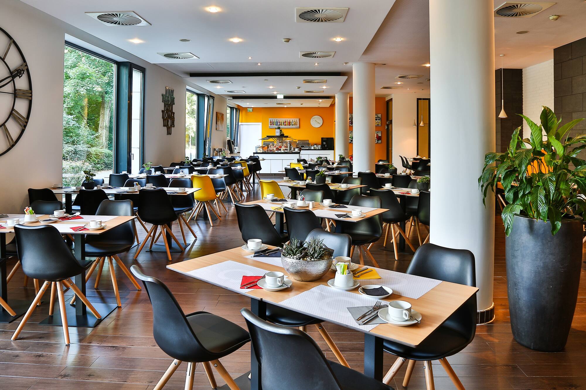 Modern restaurant with set tables, black chairs, large windows, and buffet.