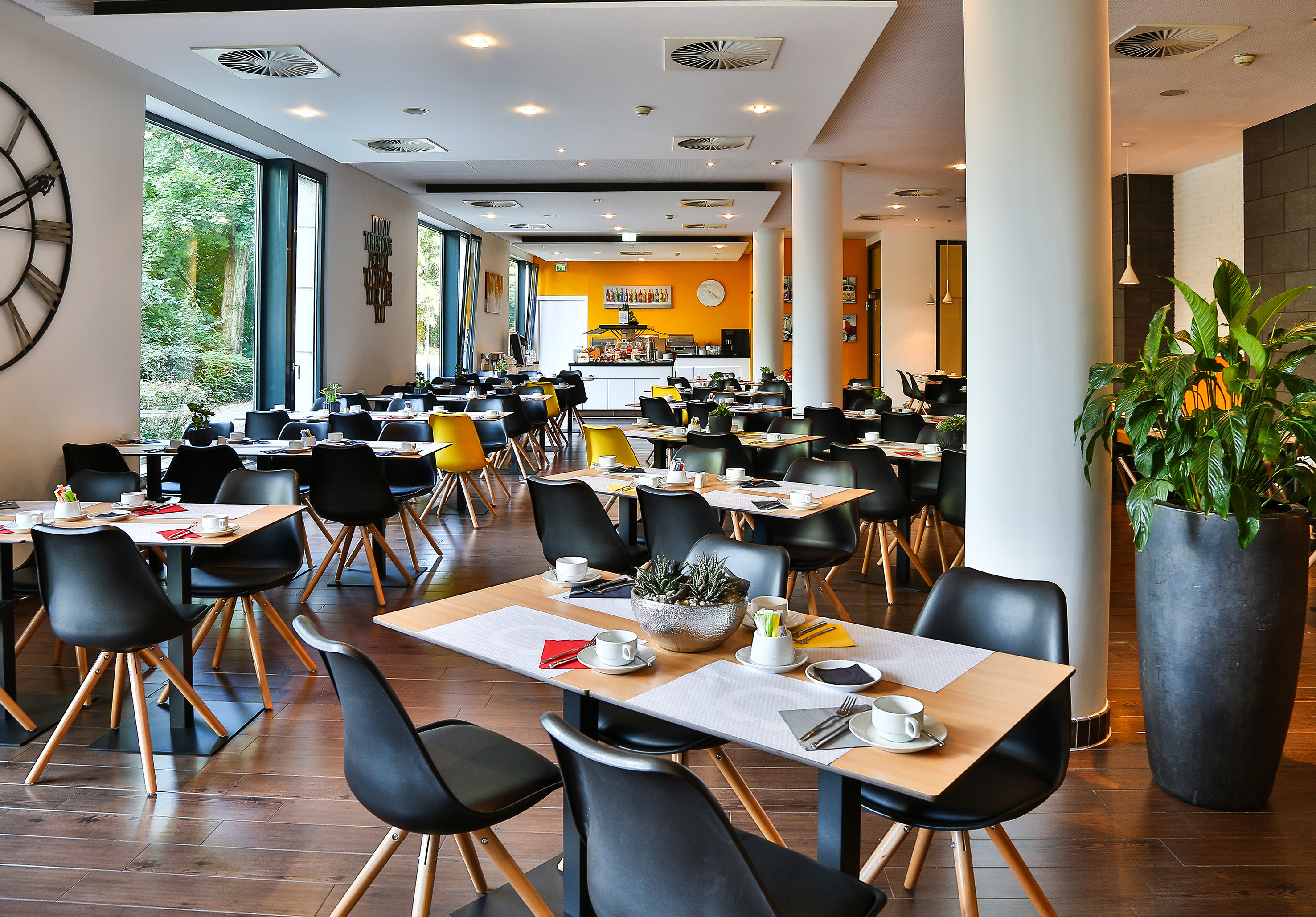 Modern restaurant with set tables, black chairs, large windows, and buffet.