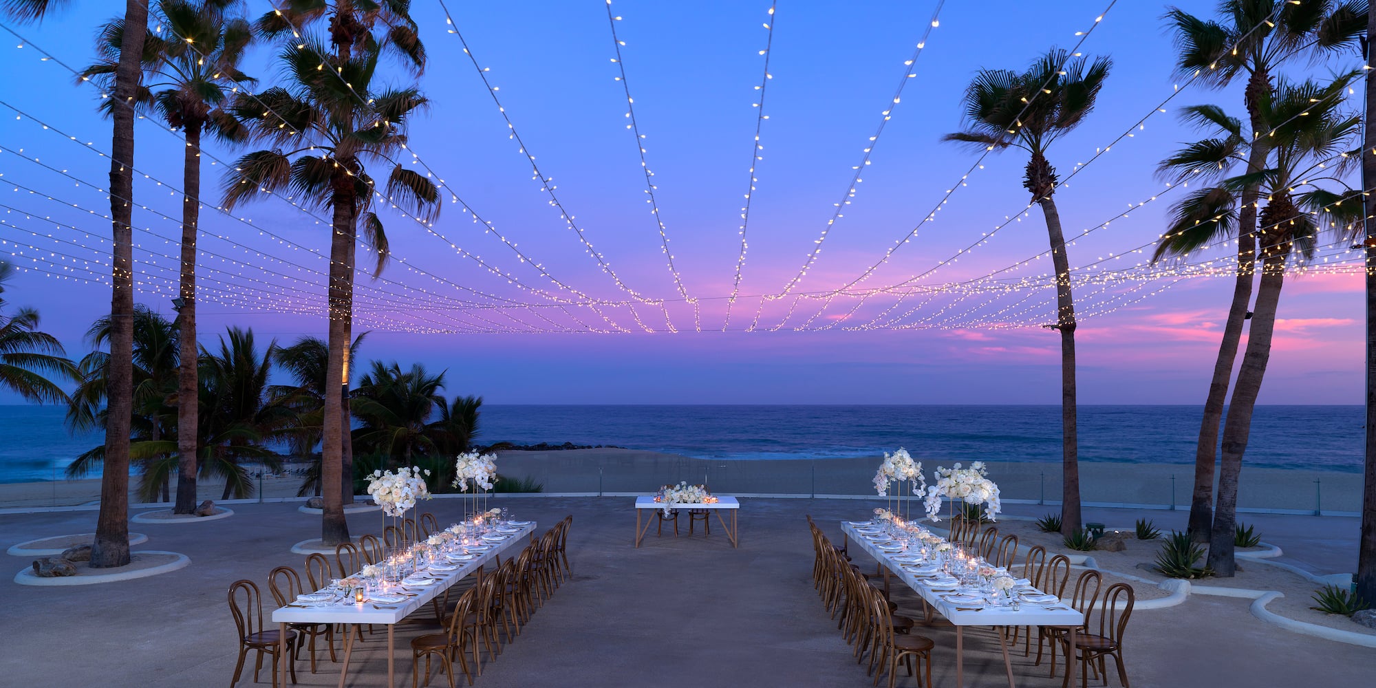 a long table set up with white flowers and candles on it