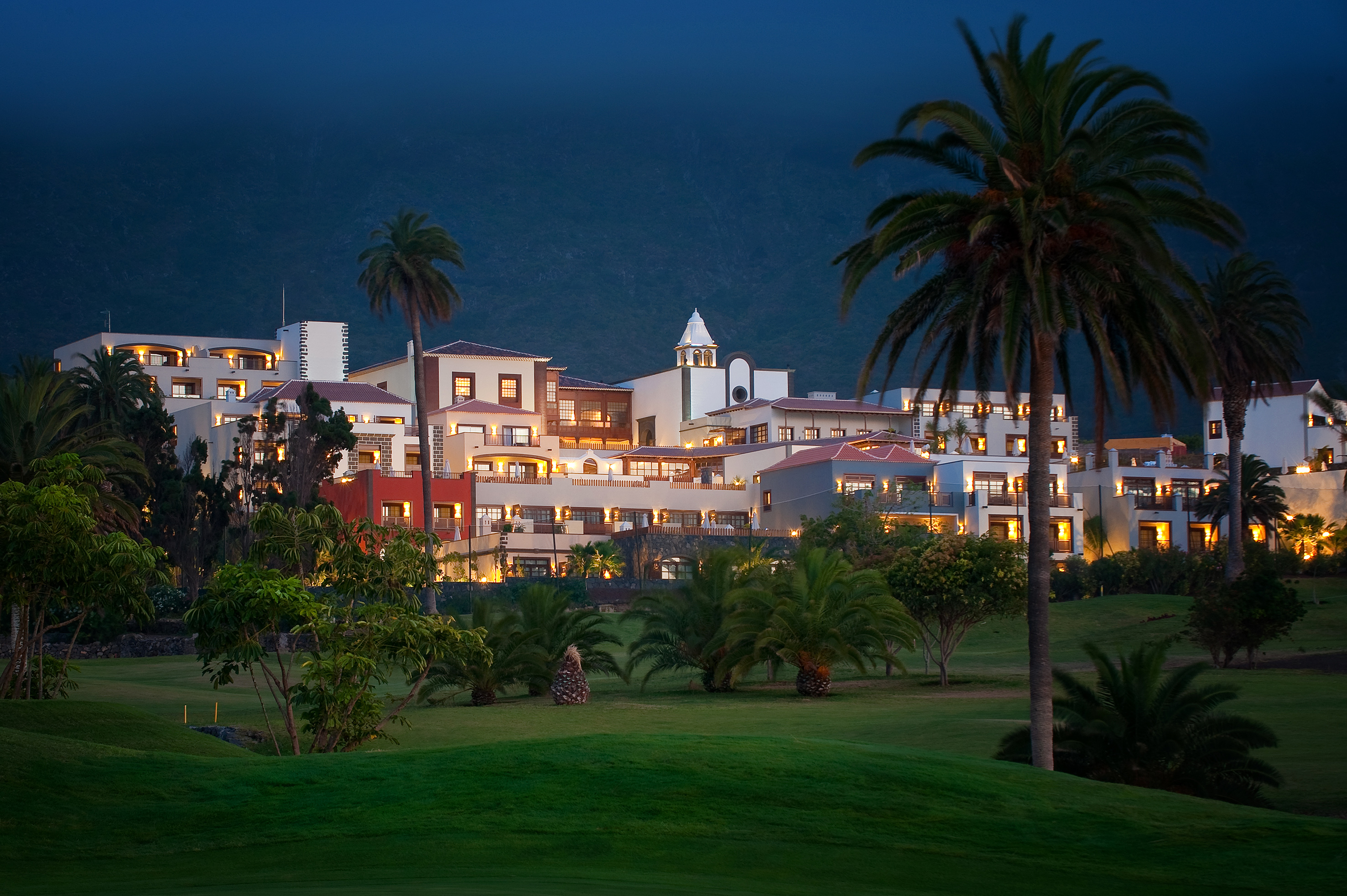 Illuminated resort with palm trees and a golf course at night.