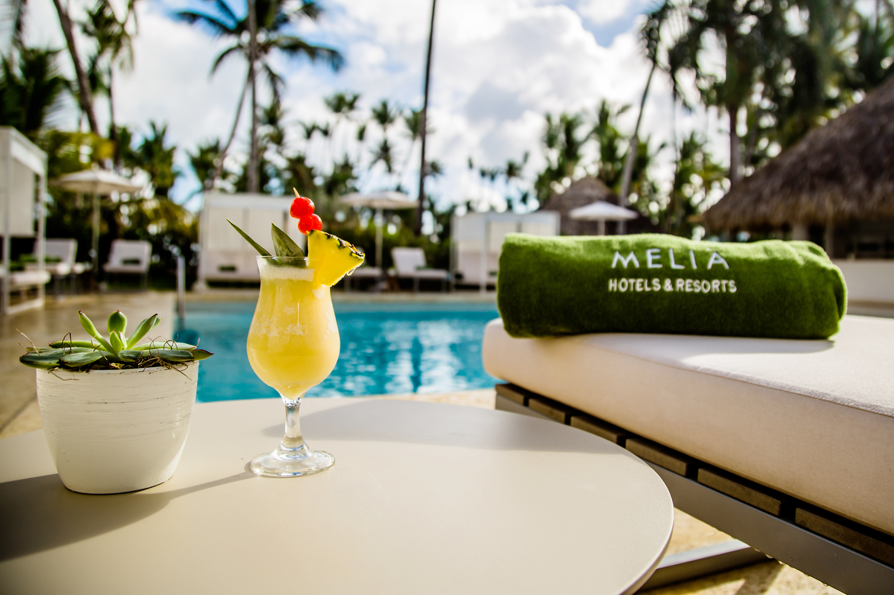 Tropical cocktail, Melia Hotels & Resorts towel, poolside, palm trees.