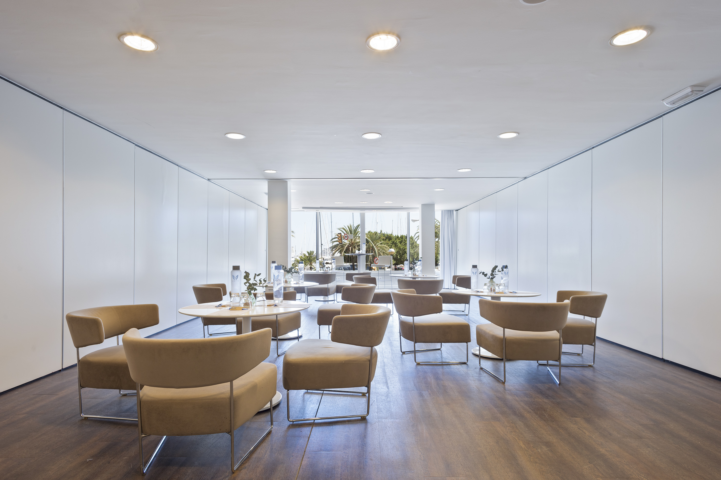 Modern conference room with beige chairs, white tables, and waterfront view.