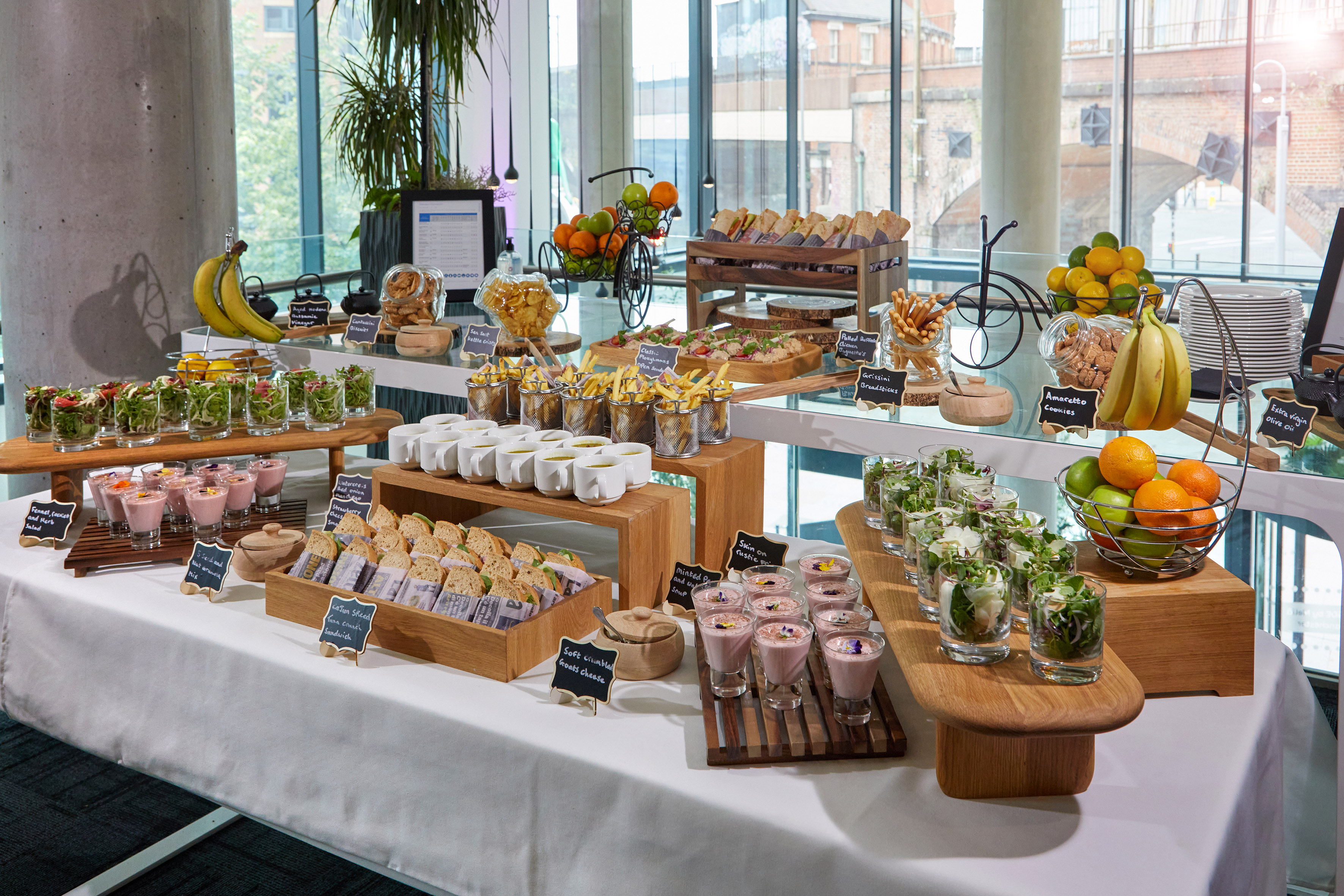 Elegant buffet spread with individual salads, sandwiches, fruits, and coffee cups for event catering.