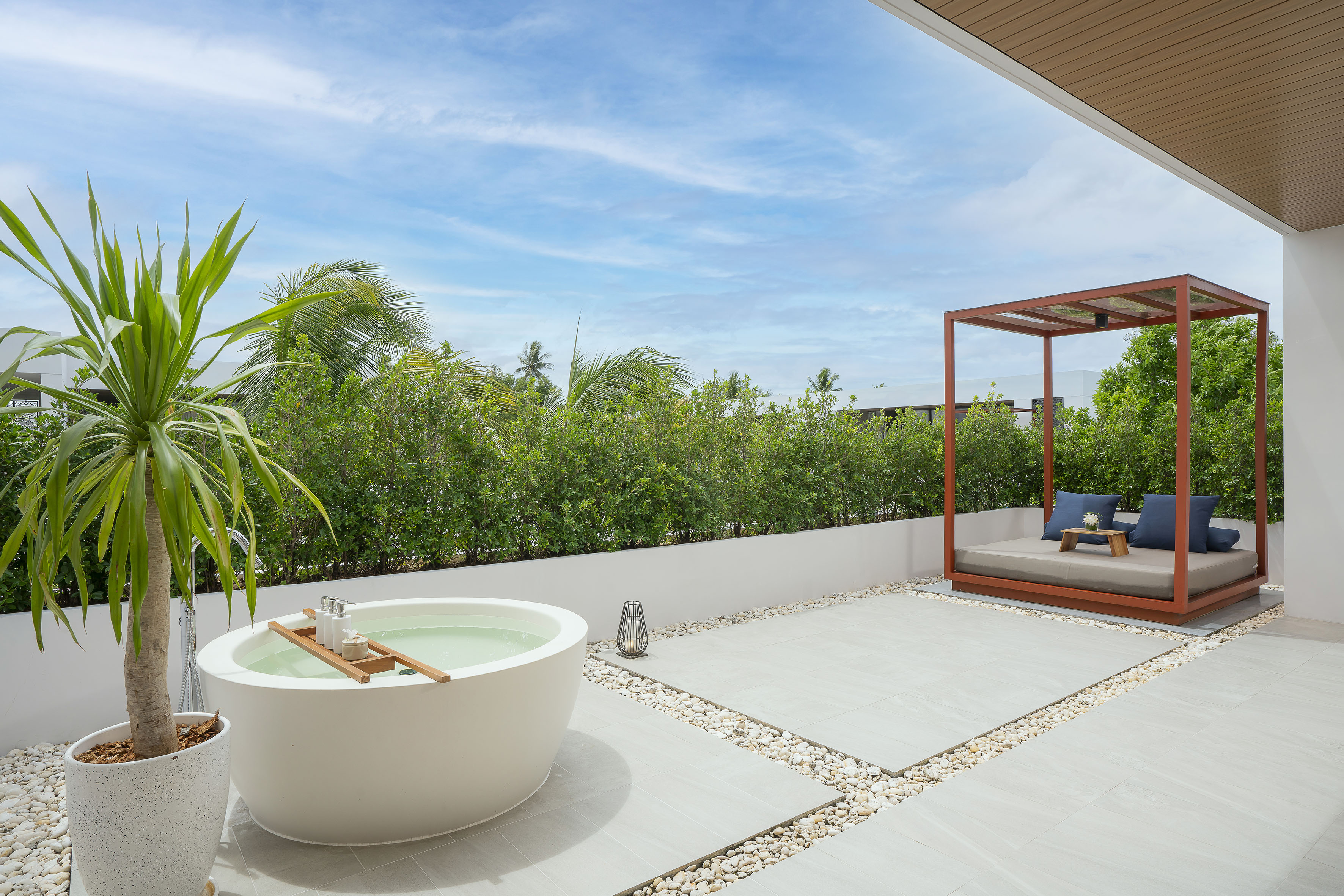 Outdoor spa terrace with freestanding tub, modern daybed, and tropical plants.