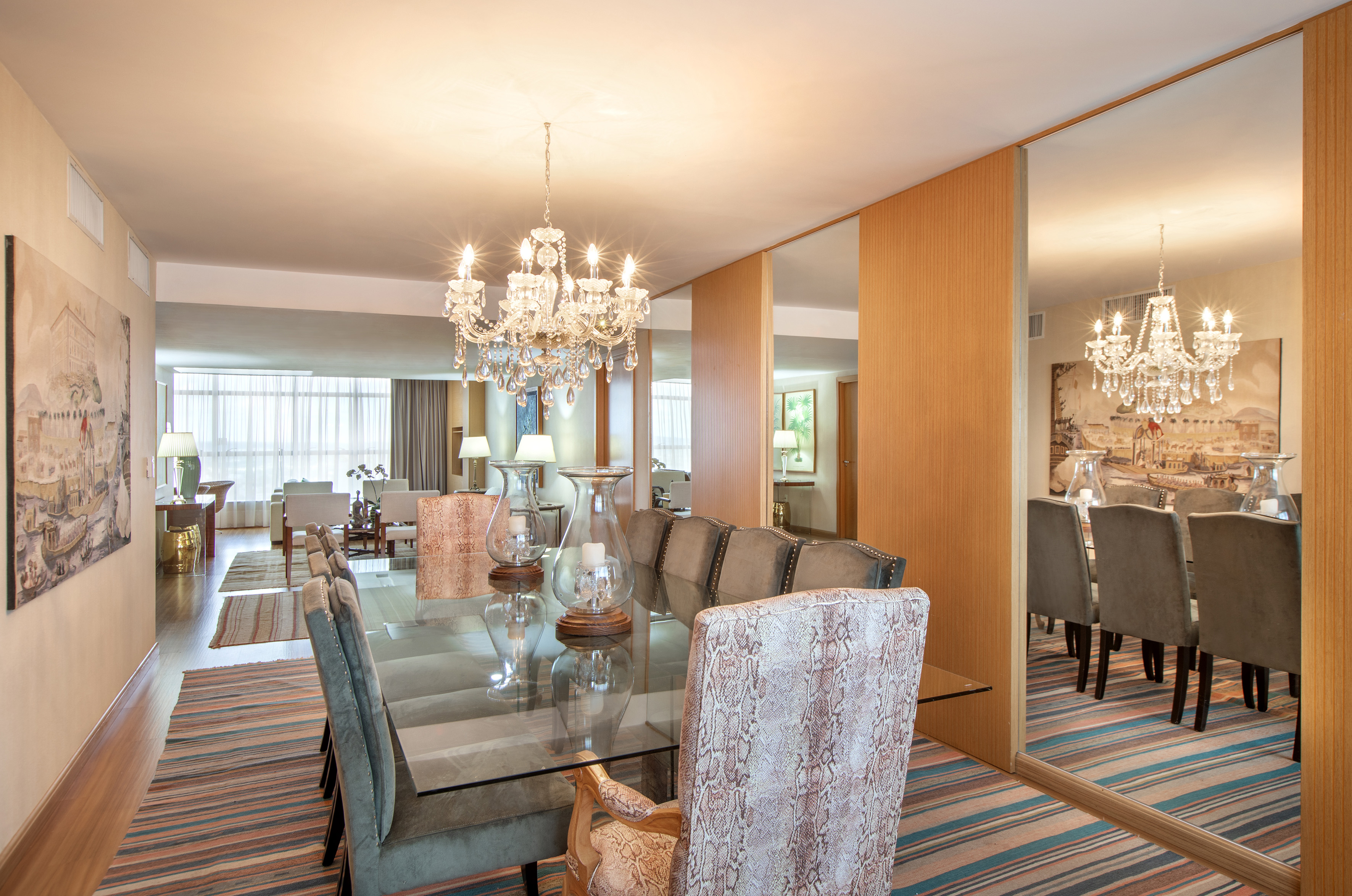 Elegant dining room with crystal chandelier, glass table, and luxurious chairs.