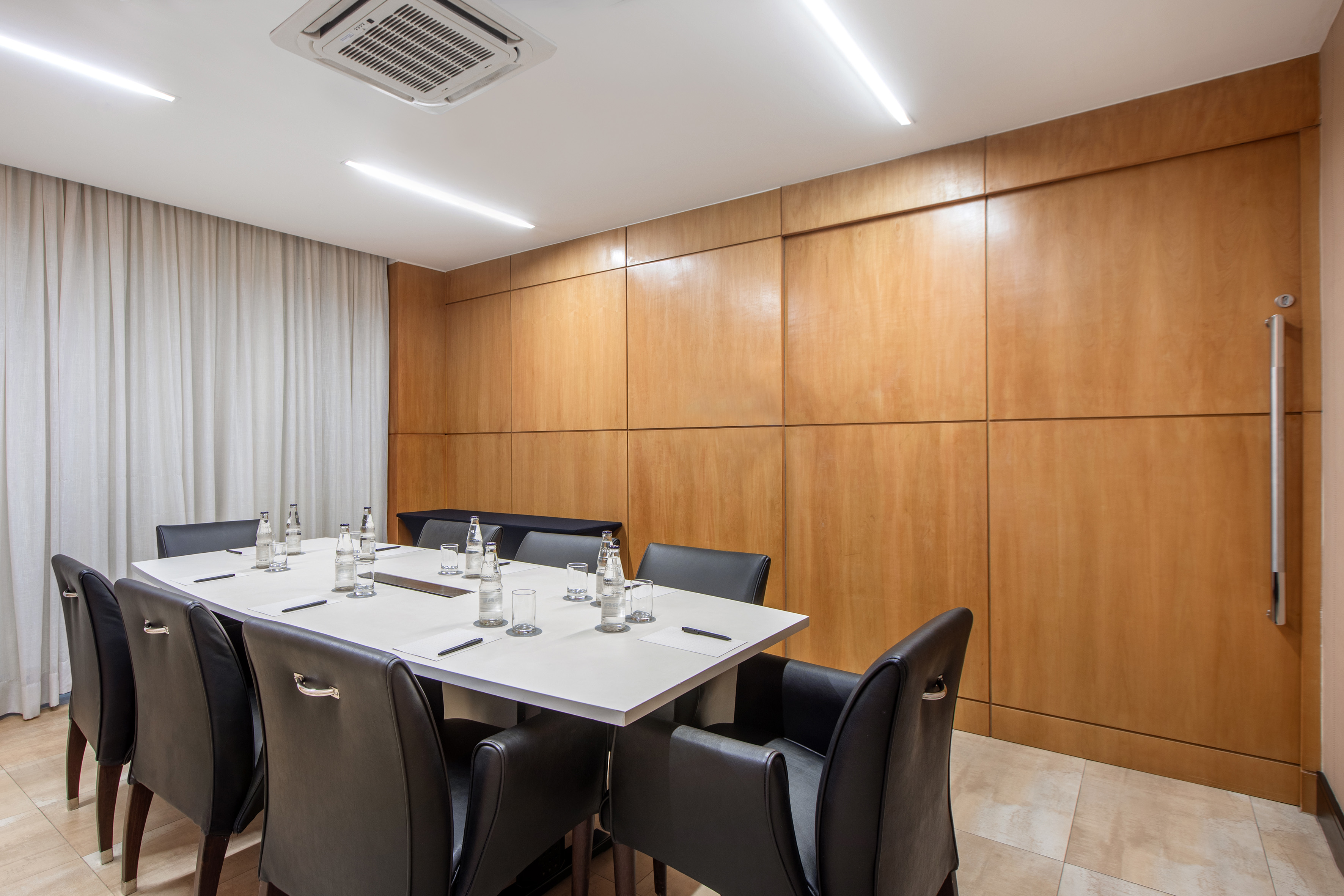 Modern conference room with long white table, black chairs, and wood-paneled walls.