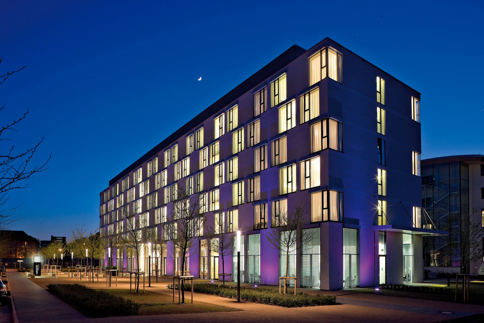 Modern Innside hotel building at night, lit windows, crescent moon.