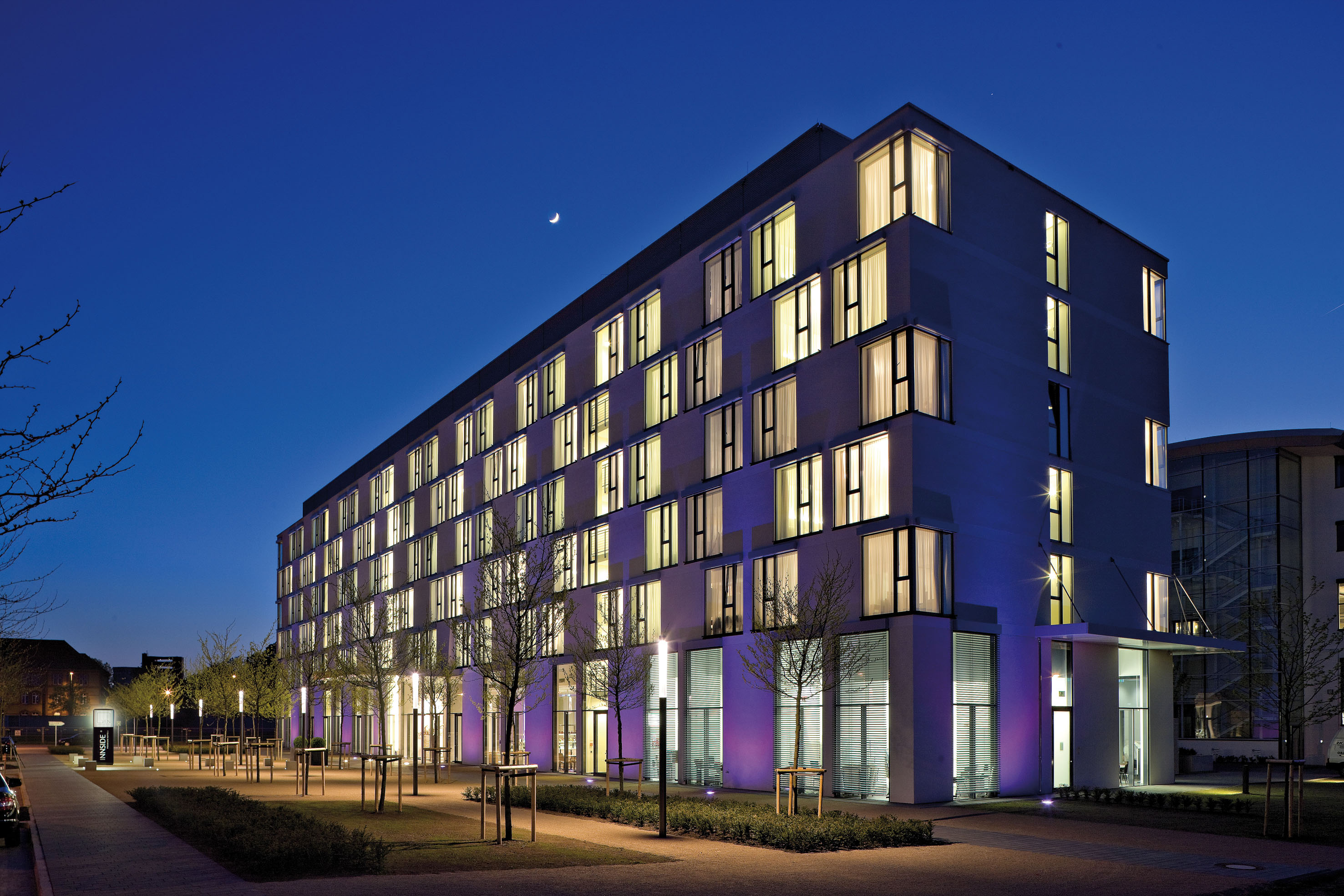 Modern Innside hotel building at night, lit windows, crescent moon.