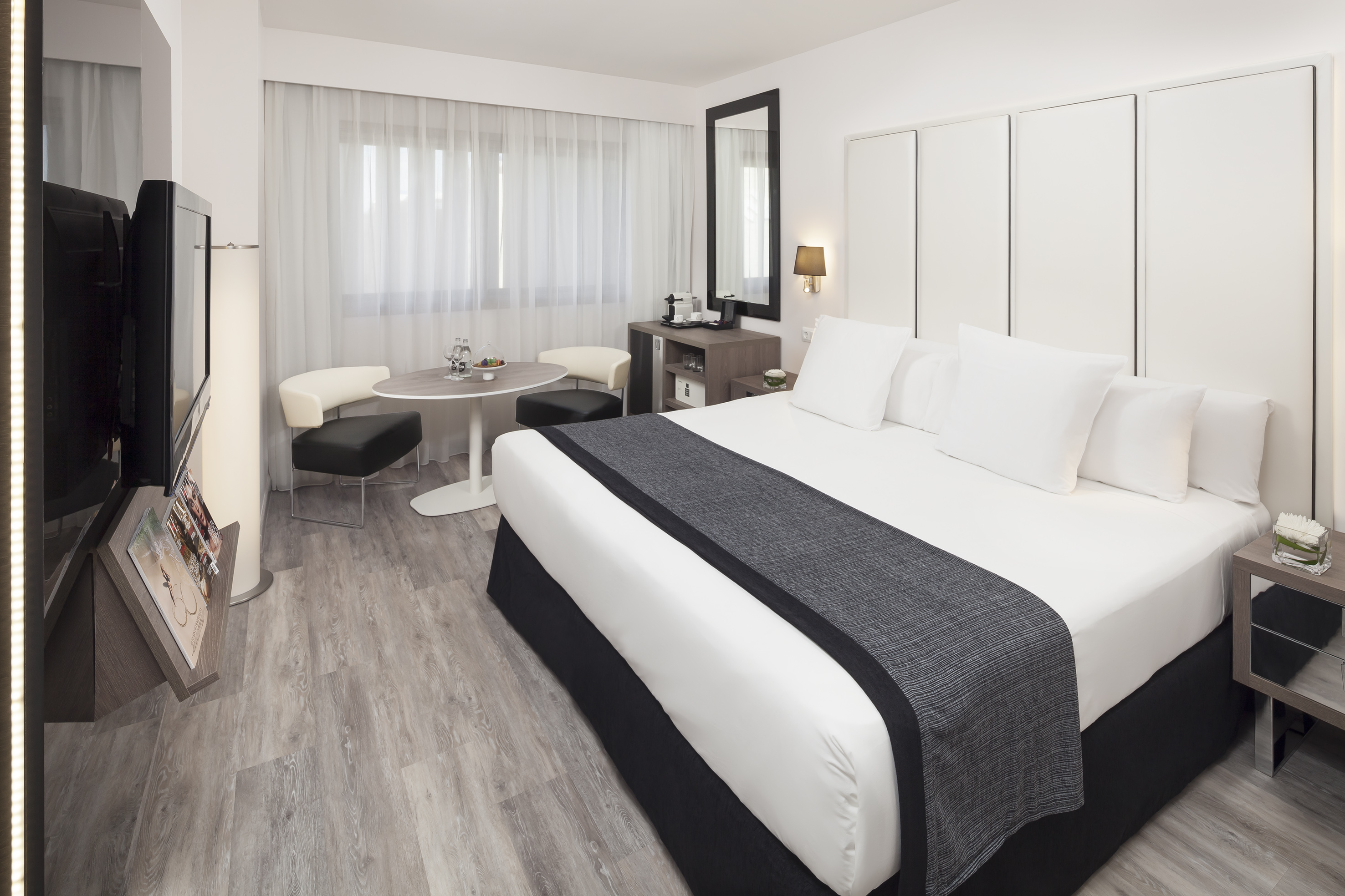 Modern hotel room with king bed, sitting area, flat-screen TV, and clean decor.