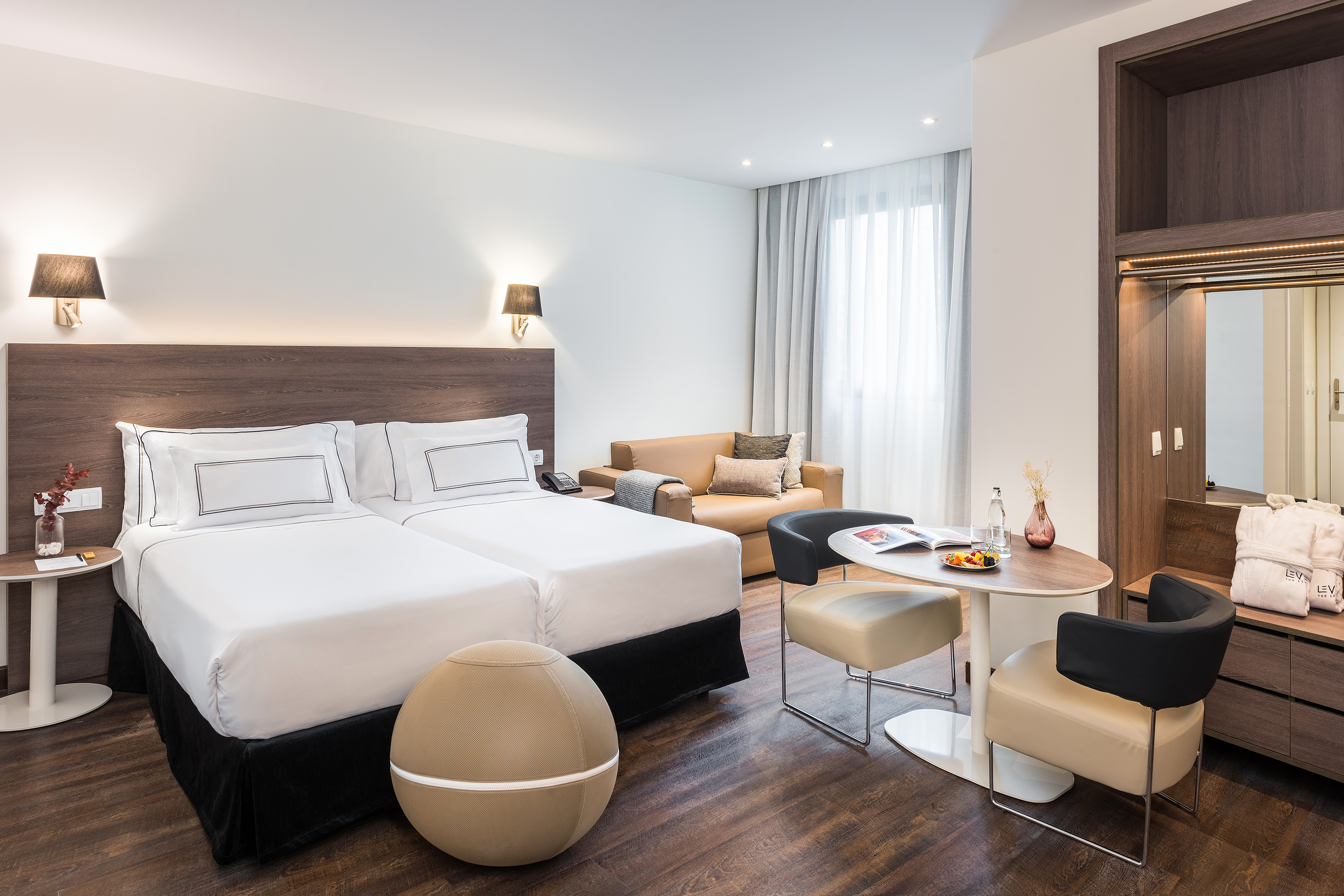 Modern hotel suite with two beds, sofa, and dining area.