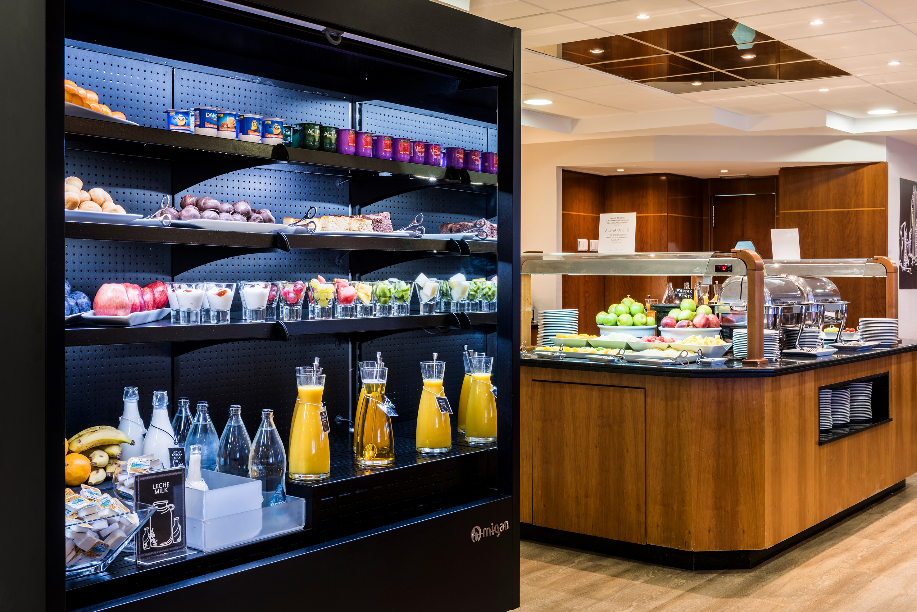 Hotel breakfast buffet with refrigerated display, pastries, fresh fruit, and juices.