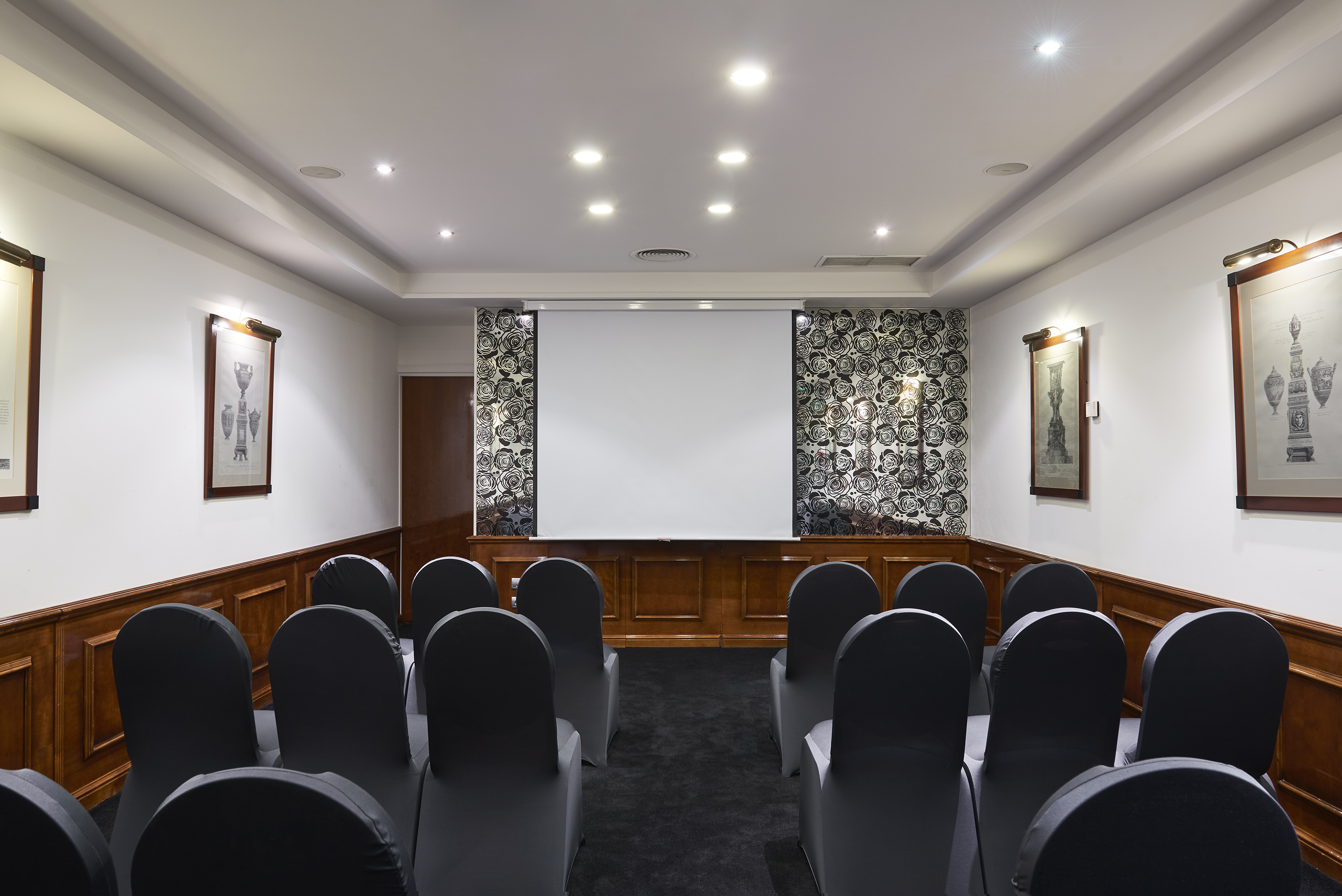Conference room with black chairs, projector screen, and wood paneling.