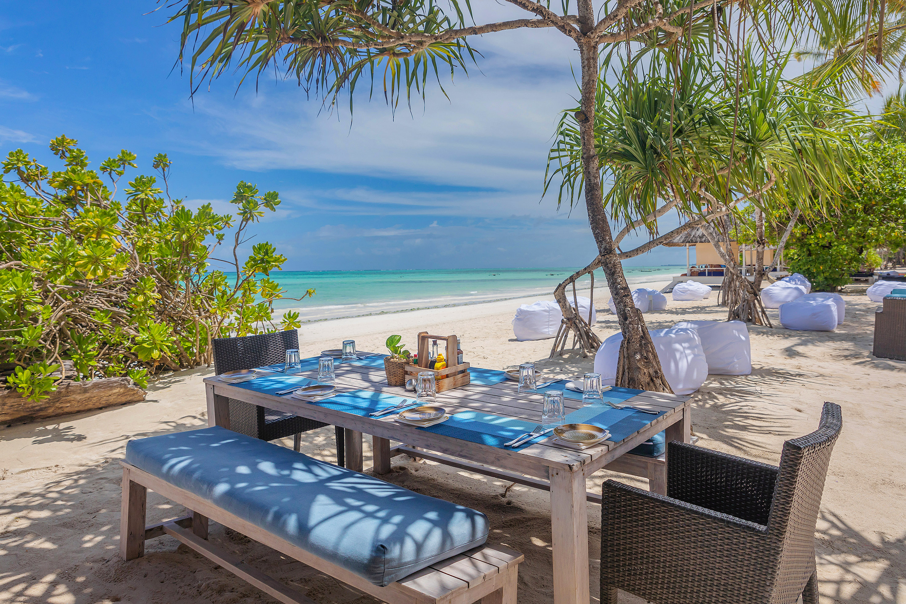 Tropical beach dining table with ocean view, shaded by palms.