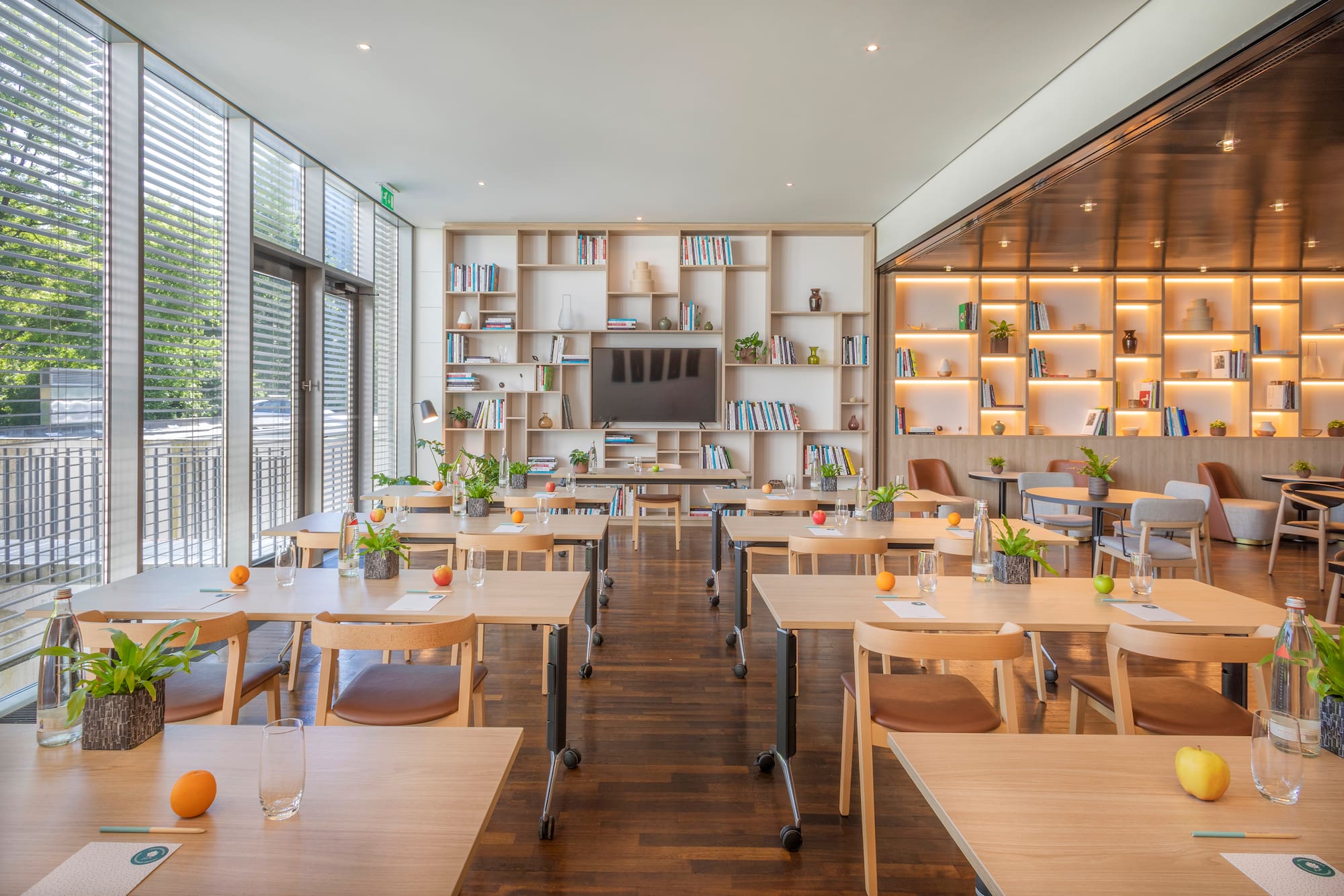 Modern training room with wood tables, natural light, bookshelves, and TV.