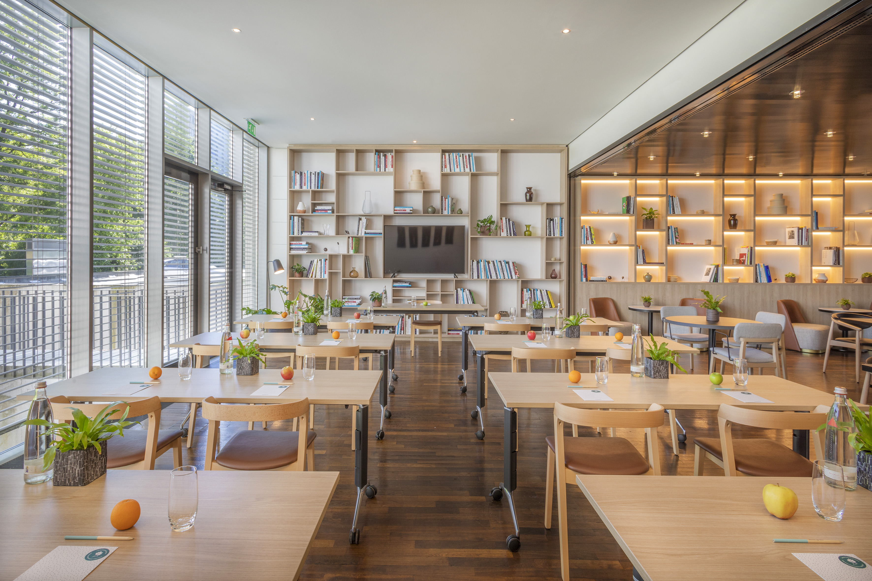 Modern training room with wood tables, natural light, bookshelves, and TV.