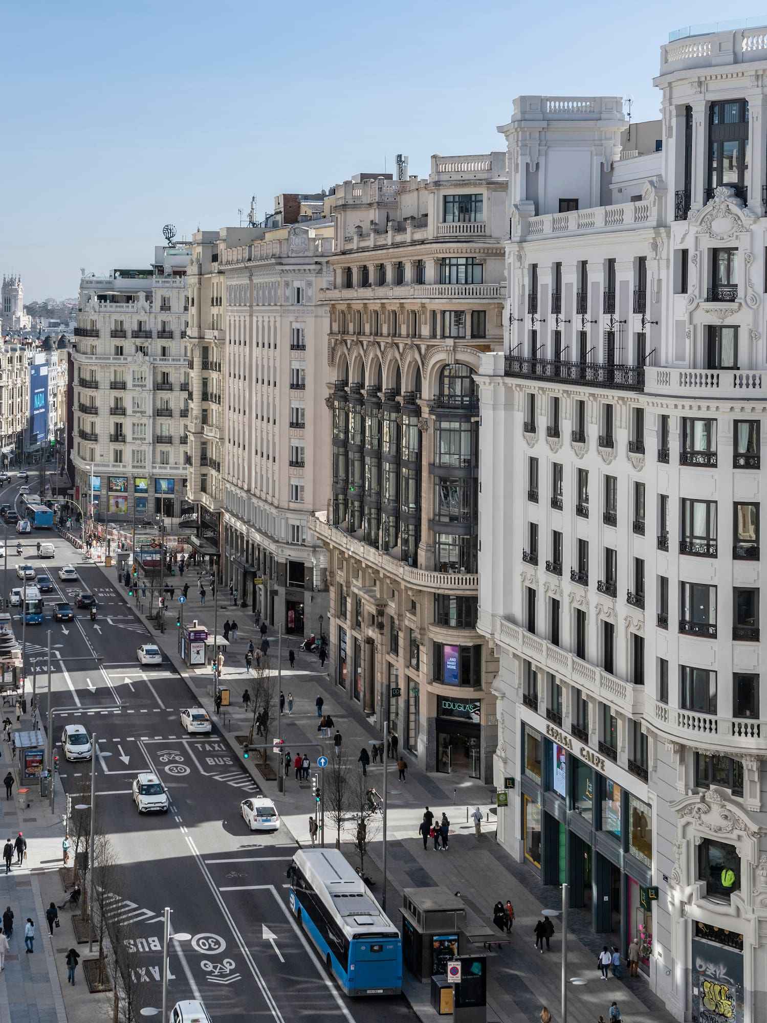 Avenida Gran Vía, Madrid: Edificios clásicos, coches, buses y peatones en la calle.