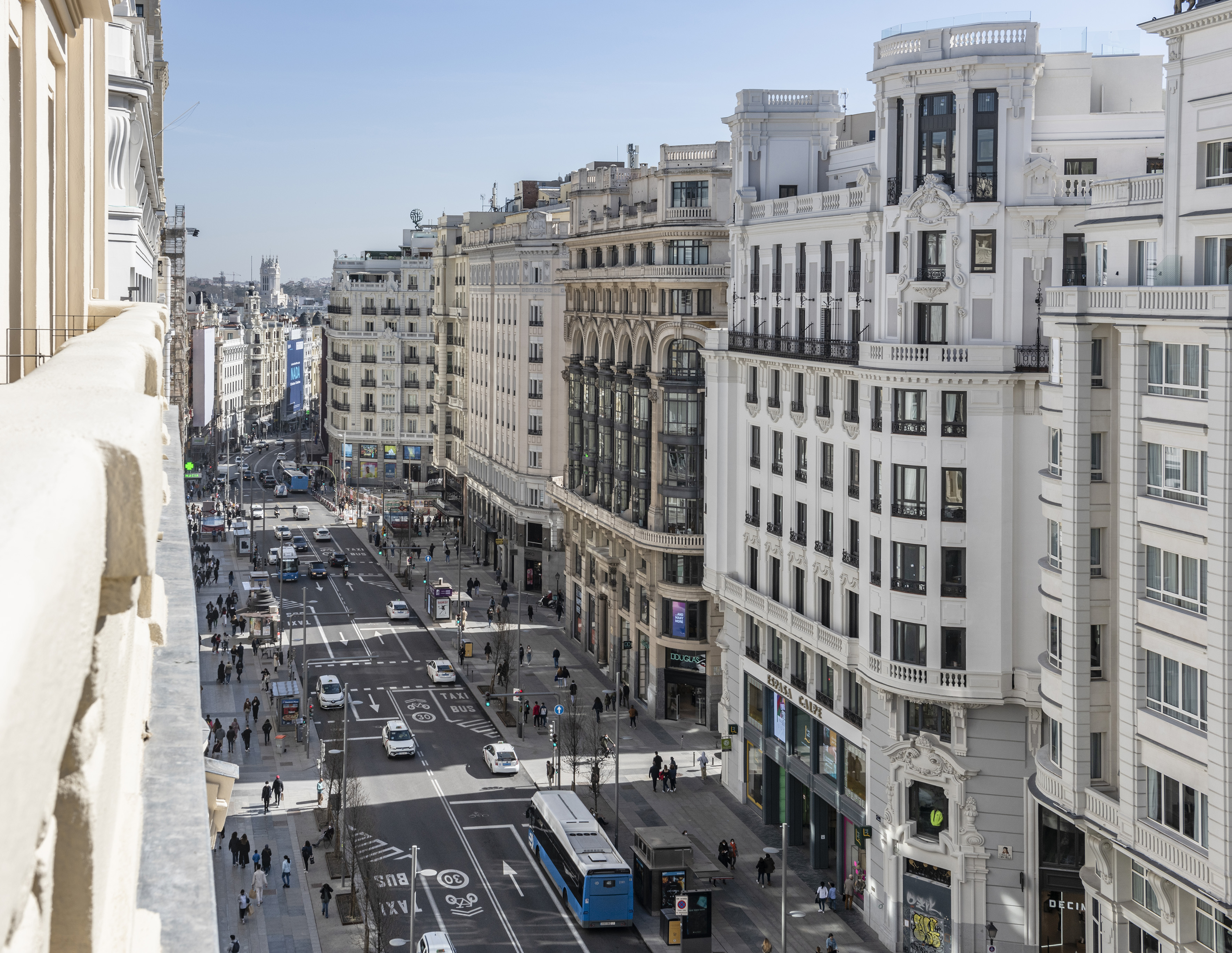 Avenida Gran Vía, Madrid: Edificios clásicos, coches, buses y peatones en la calle.