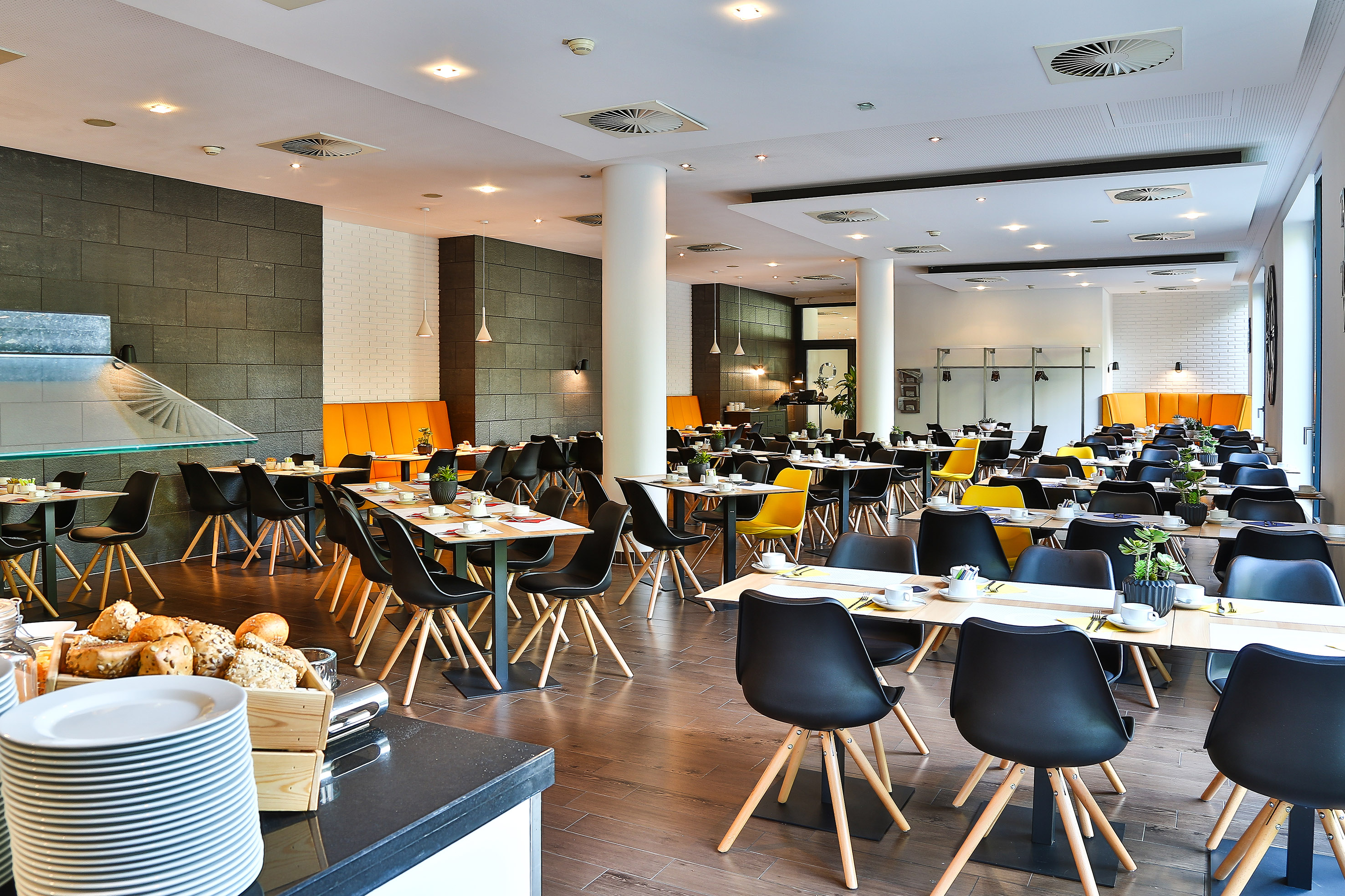 Modern hotel dining room with black chairs, orange booths, and set tables.