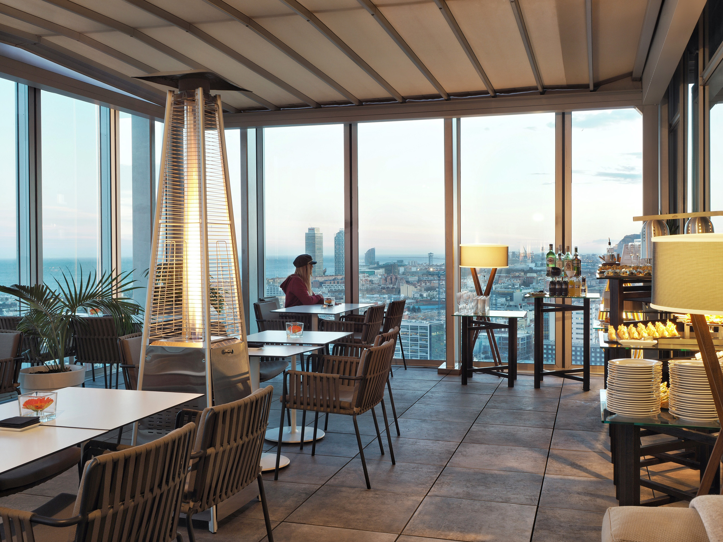 Rooftop restaurant terrace with panoramic city, ocean views, patio heater, and seating.